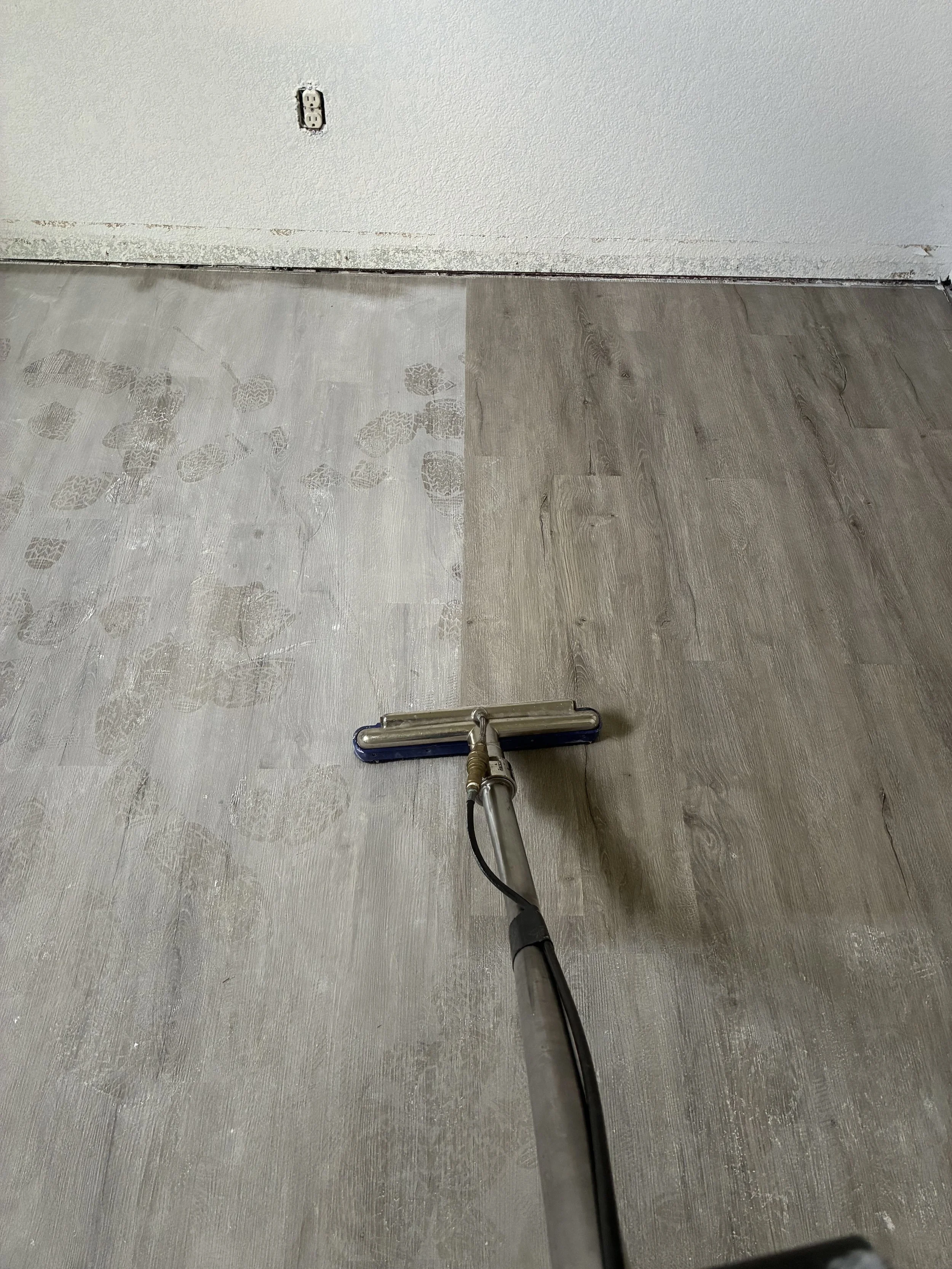 Floor being cleaned, with a portion of the floor showing footprints or dirt marks, and a floor cleaning machine in the foreground.