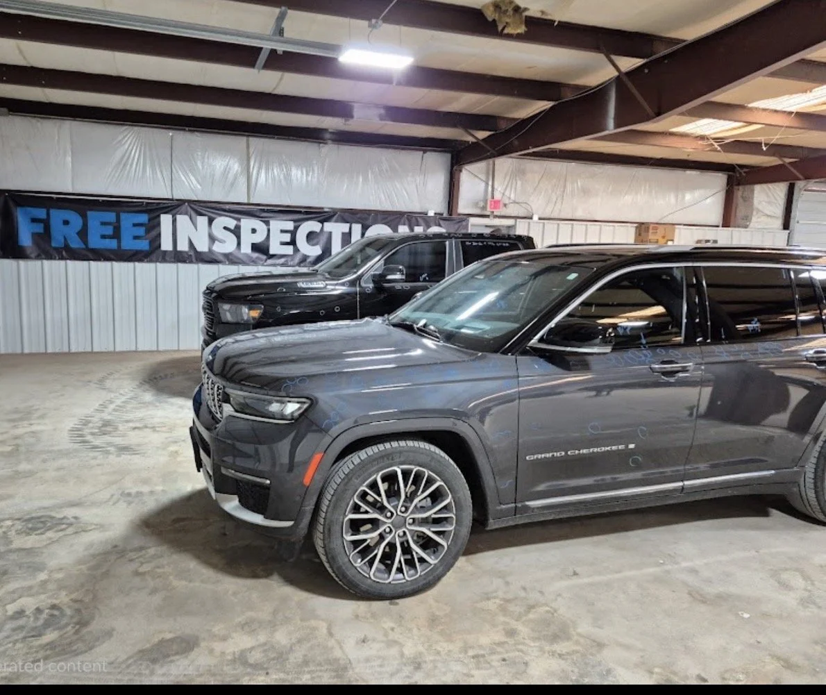 Two black SUVs parked inside a warehouse with a sign that says 'FREE INSPECTION' in the background.