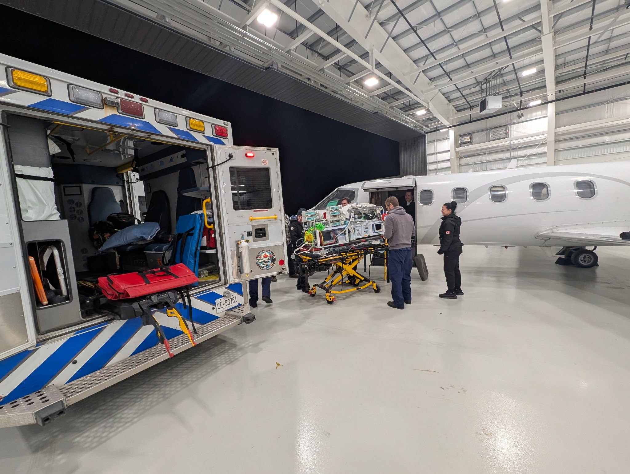 Medical team preparing equipment on a stretcher next to a private jet in hangar.
