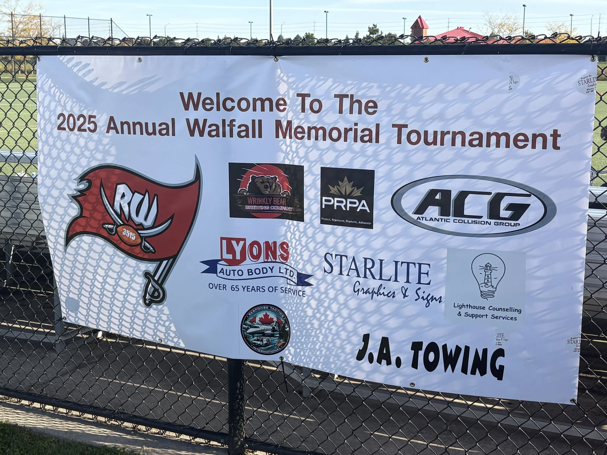 Banner for the 2025 Annual Walfall Memorial Tournament featuring sponsor logos and text on a chain-link fence.
