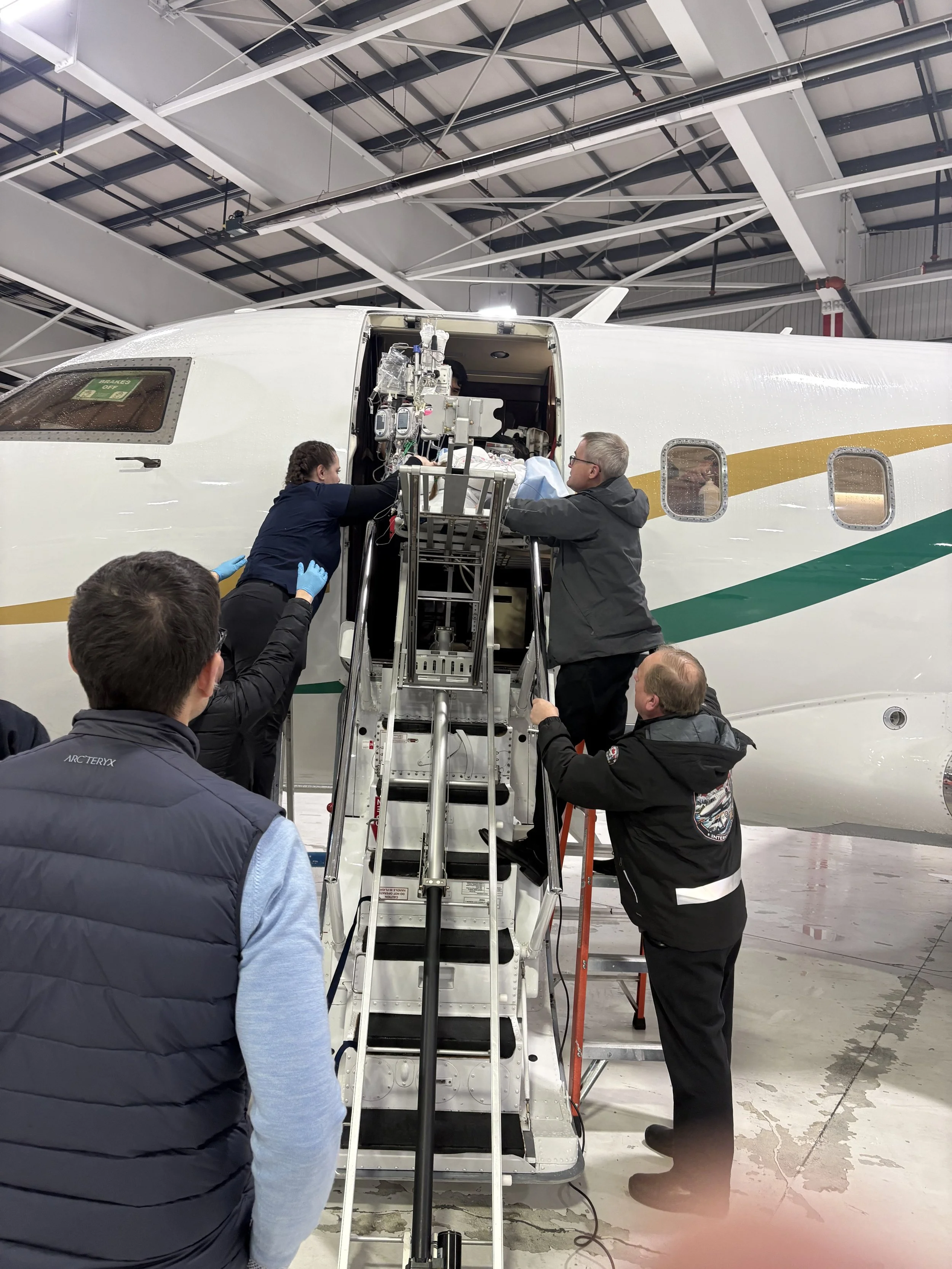 A group of people working on the nose section of a large airplane inside a hangar, with some individuals on a mobile staircase and others on the ground.