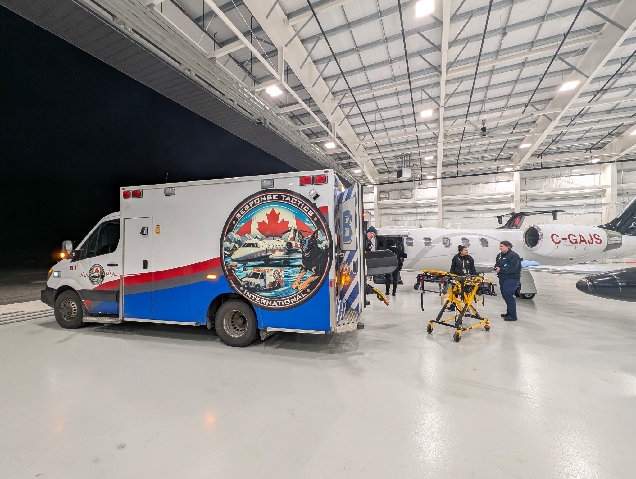 Emergency response vehicle at an airport hangar with personnel preparing a private jet and medical equipment.