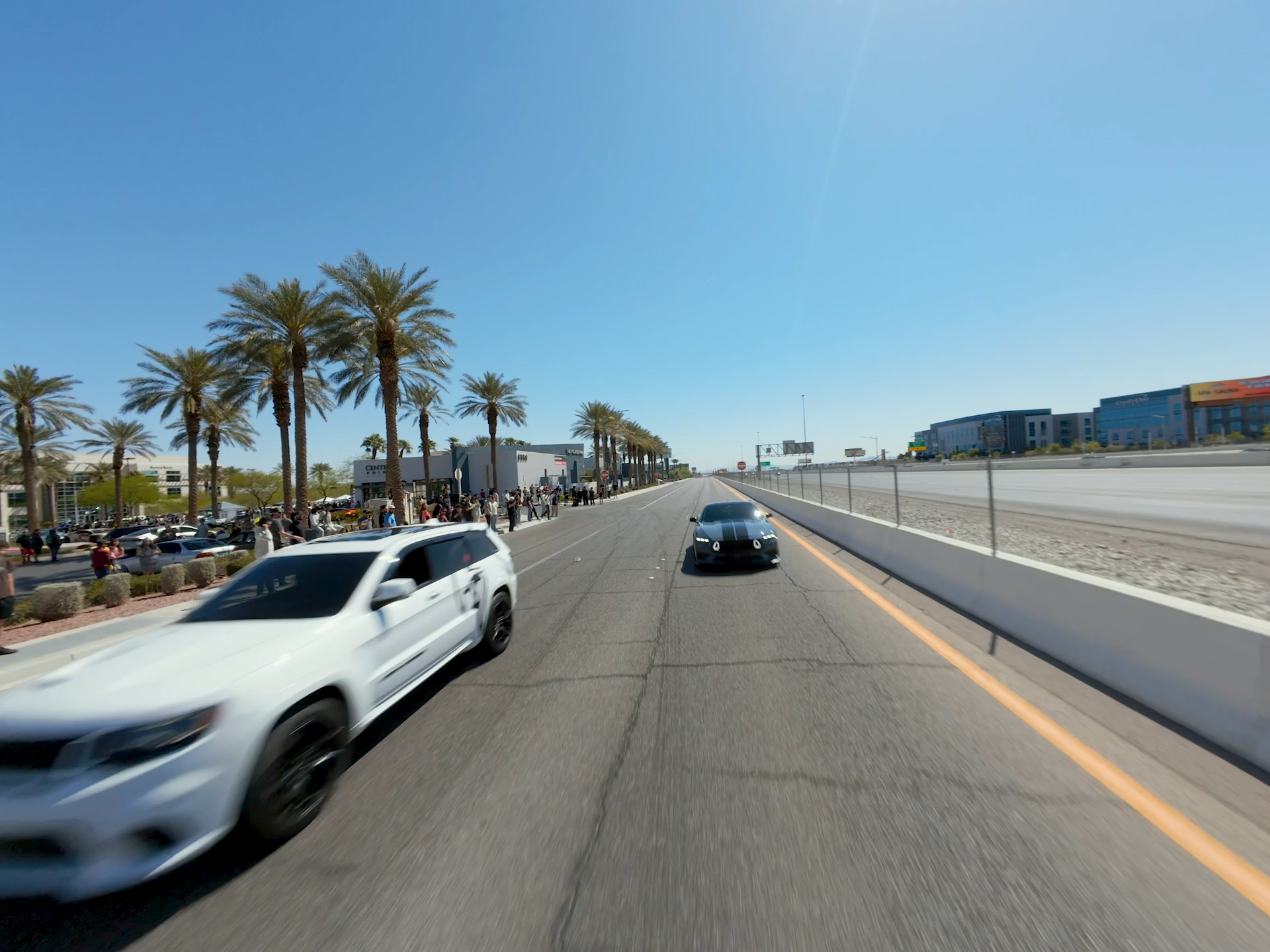 Moving white sports car on a city street with palm trees and buildings in the background