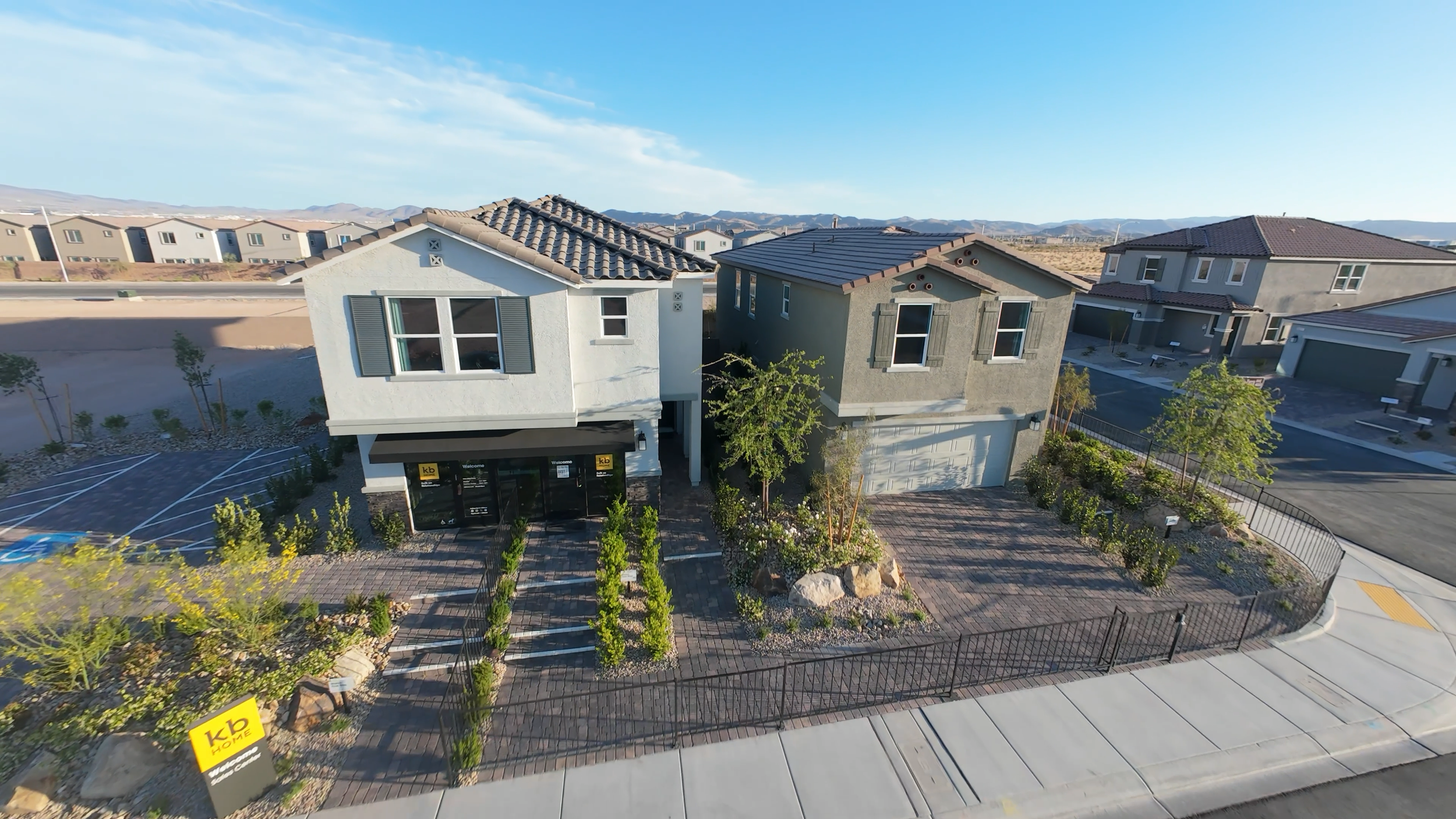 Residential neighborhood with modern two-story houses, landscaped front yards, trees, and a clear blue sky.