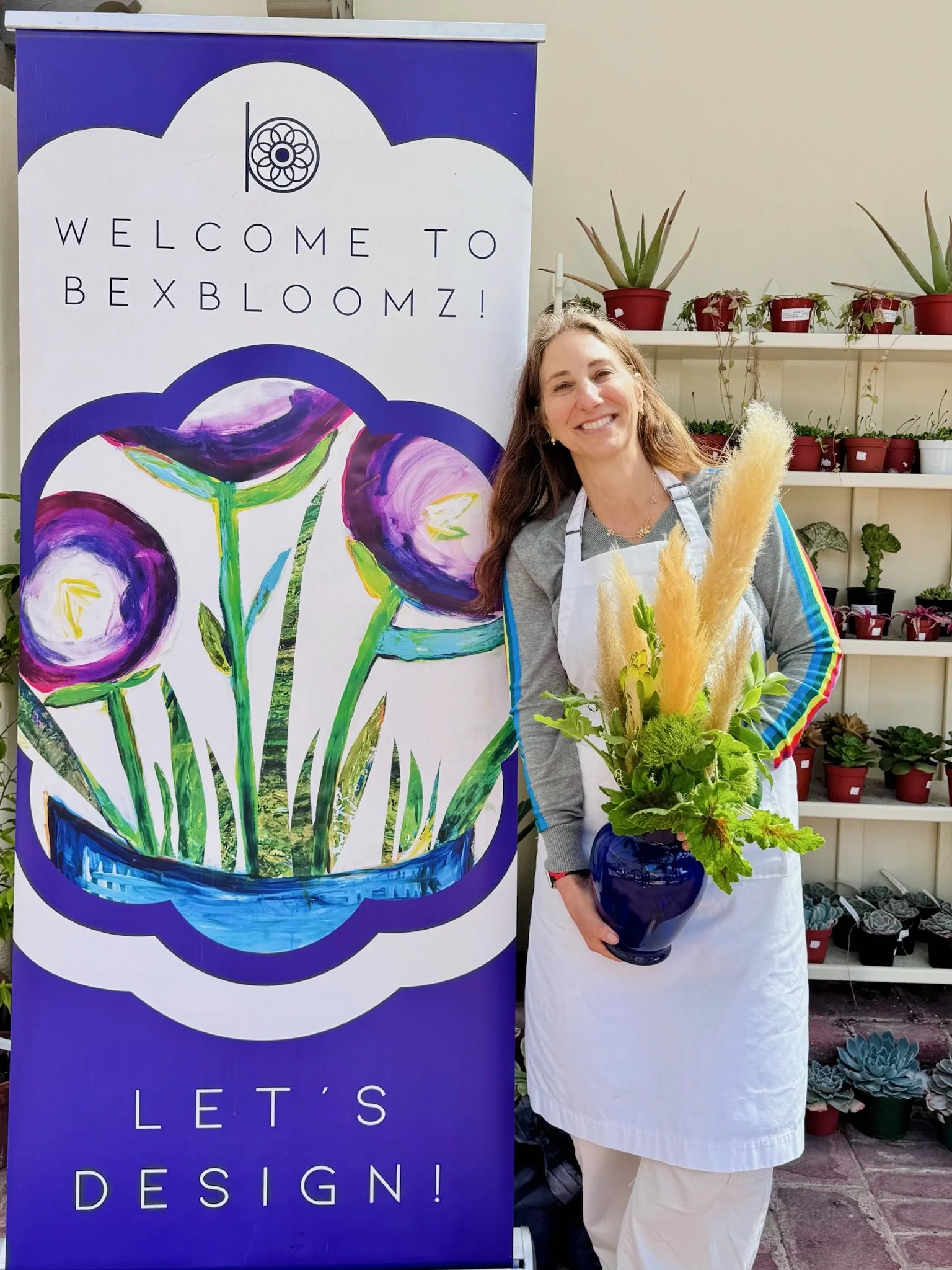 Becky next to BEXBLOOMZ sign holding an arrangement