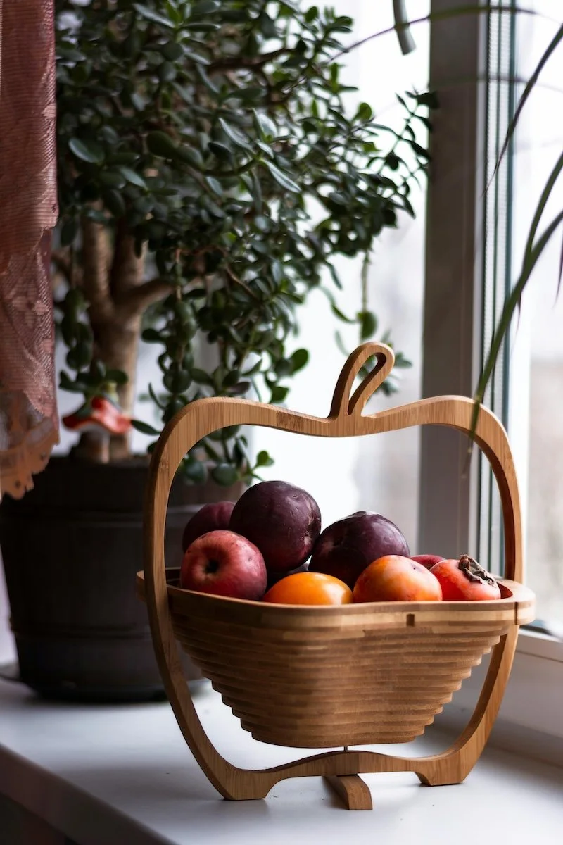 Fast forward nutrition -  A wooden apple-shaped basket filled with apples and surrounded by potted plants on a windowsill.