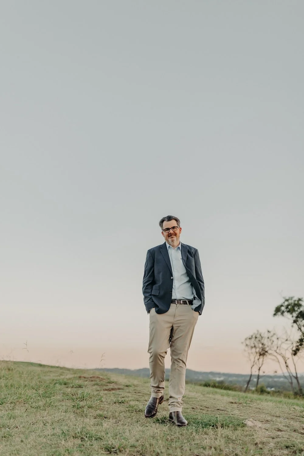Nutritionist Jon Bowly smiling in open field at sunset, hands in pockets