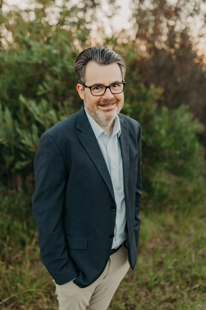 Nutritionist Jon Bowly smiling in open field at sunset, hands in pockets