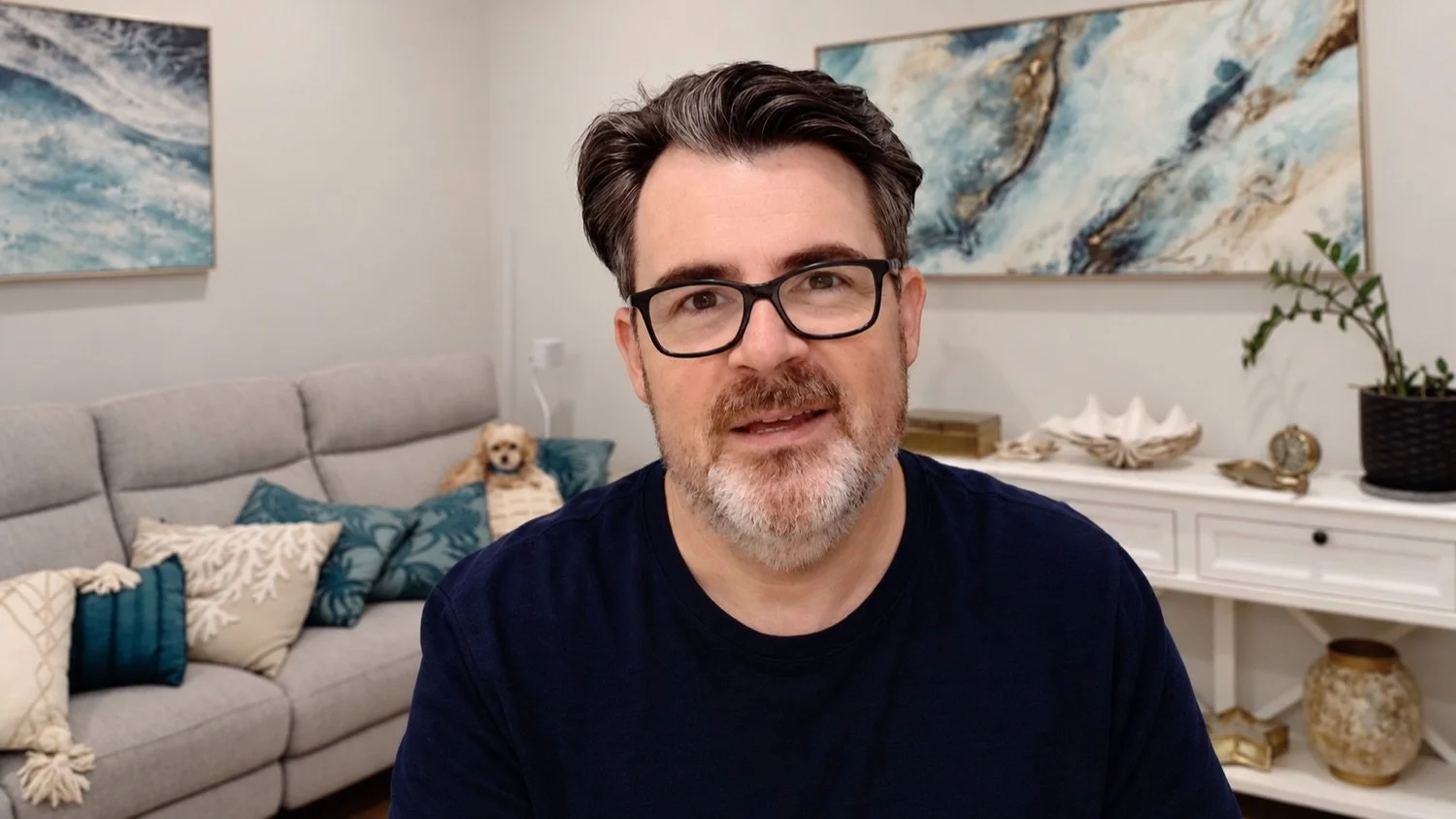 Jon Bowly smiling, with his dog Leo on the couch behind him