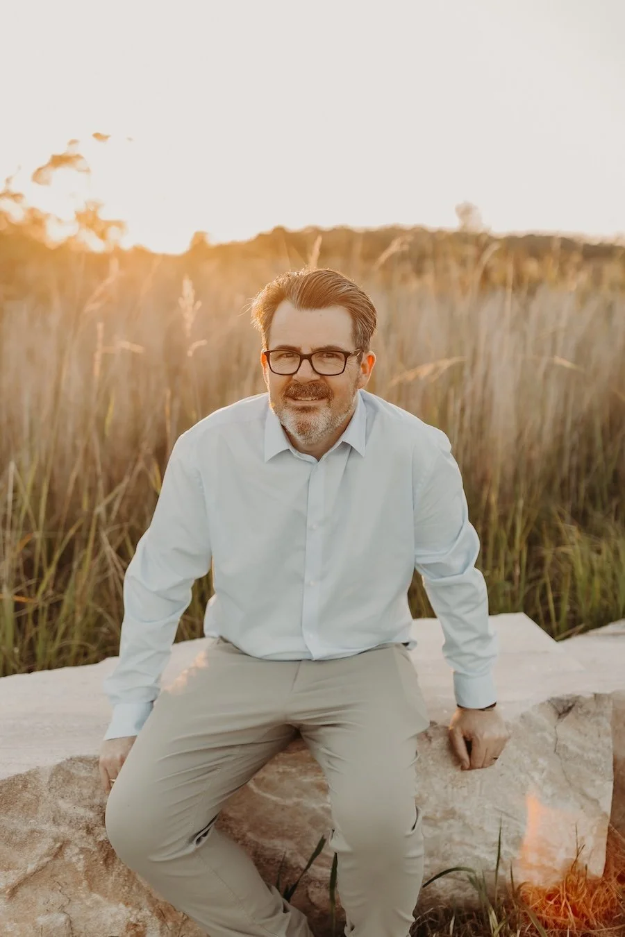 Nutritionist for weight loss jon bowly sitting on a stone bench outdoors during sunset, with tall grass in the background.