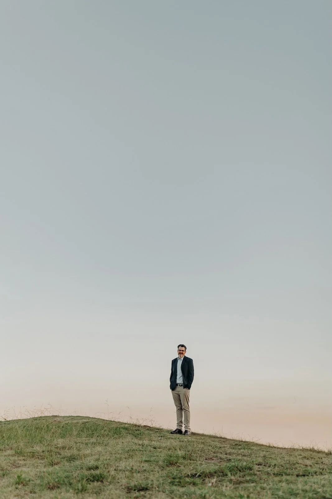 weight loss nutritionist jon bowly in a suit standing on a grassy hill under a clear sky.