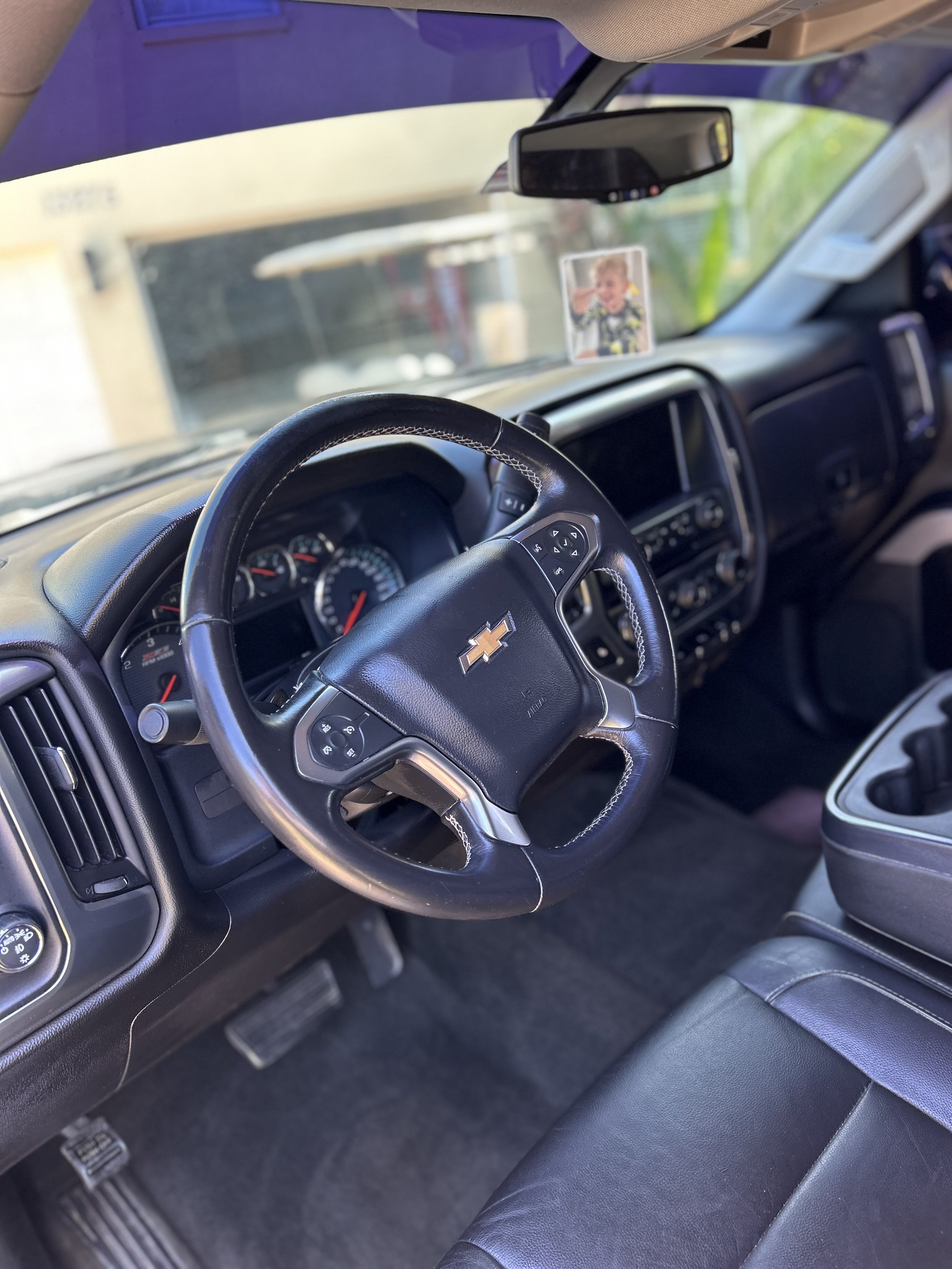 Interior of a Chevrolet truck with a steering wheel, dashboard, gear shift, and a seat. A small photo of a boy is attached to the dashboard. The view is from the driver's side.