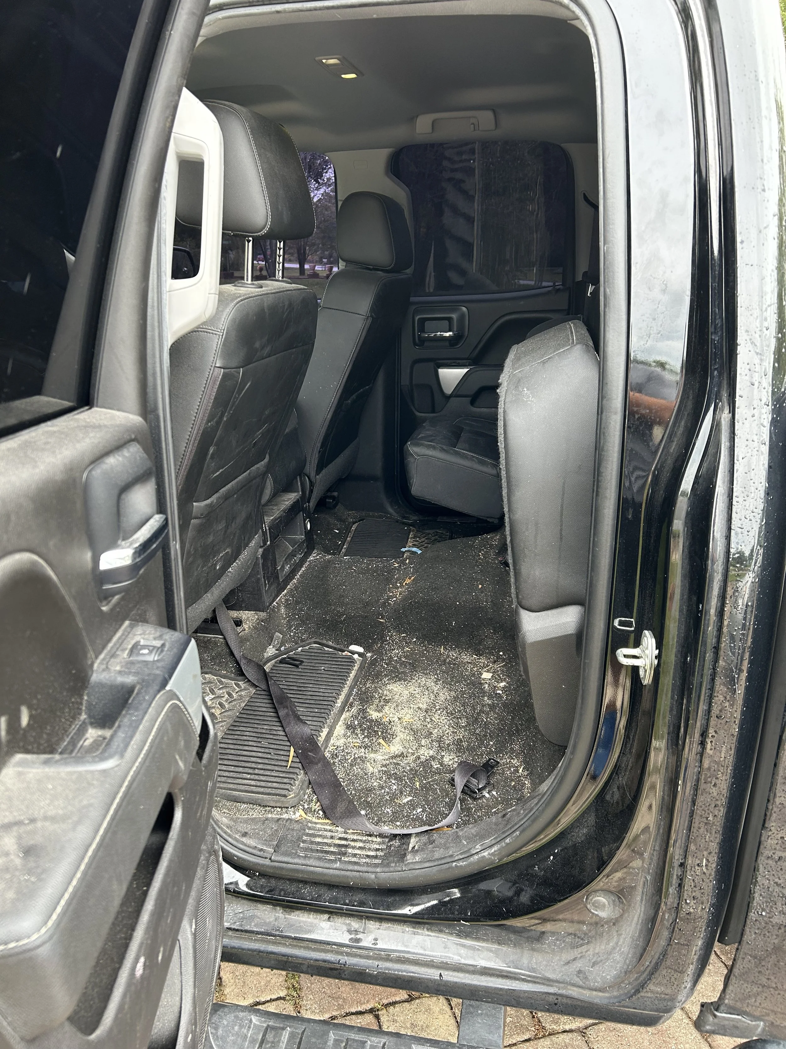 Inside the backseat area of a black SUV with dirty floor, some debris, and seat belts visible.