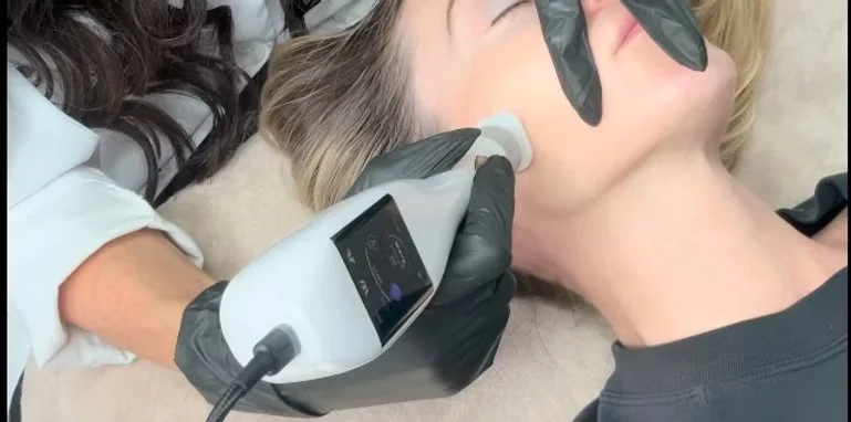 A woman receiving a jet plasma facial treatment from a professional holding a handheld skincare device on her cheek.