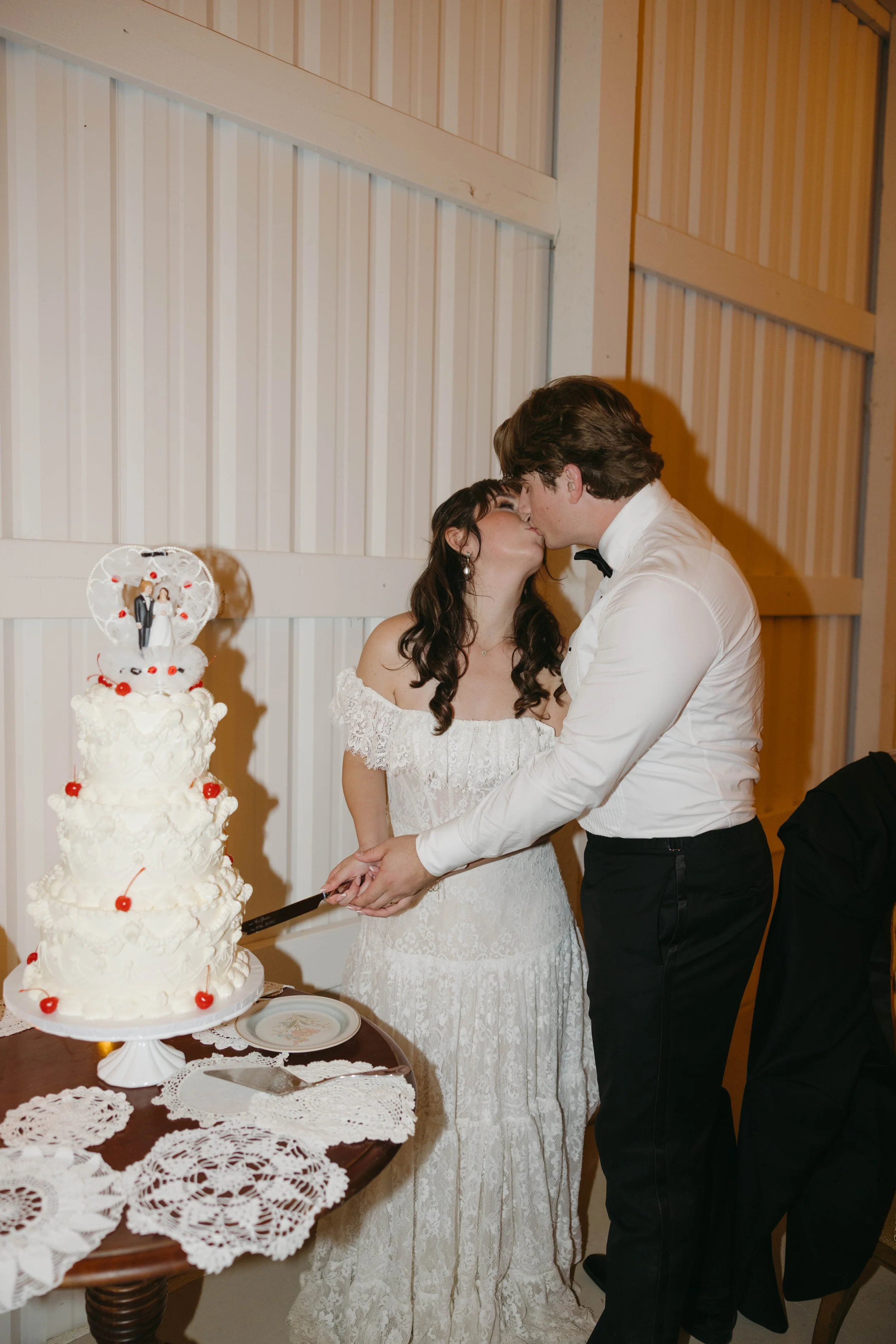 Bride and groom kissing while cutting wedding cake at reception.