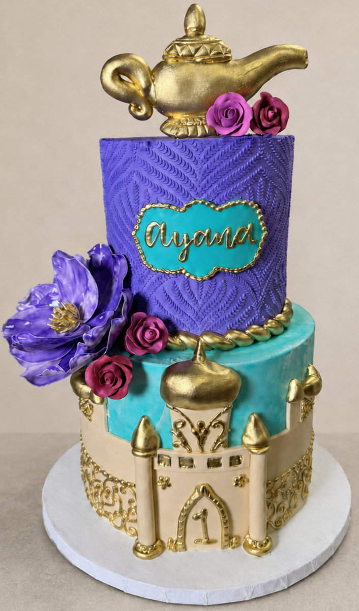 Colorful birthday cake with a princess theme, featuring purple and blue layers, gold accents, flowers, and a genie lamp topper. The cake has a sign that reads 'Ayana' and a number '1' on the front, indicating a first birthday celebration.