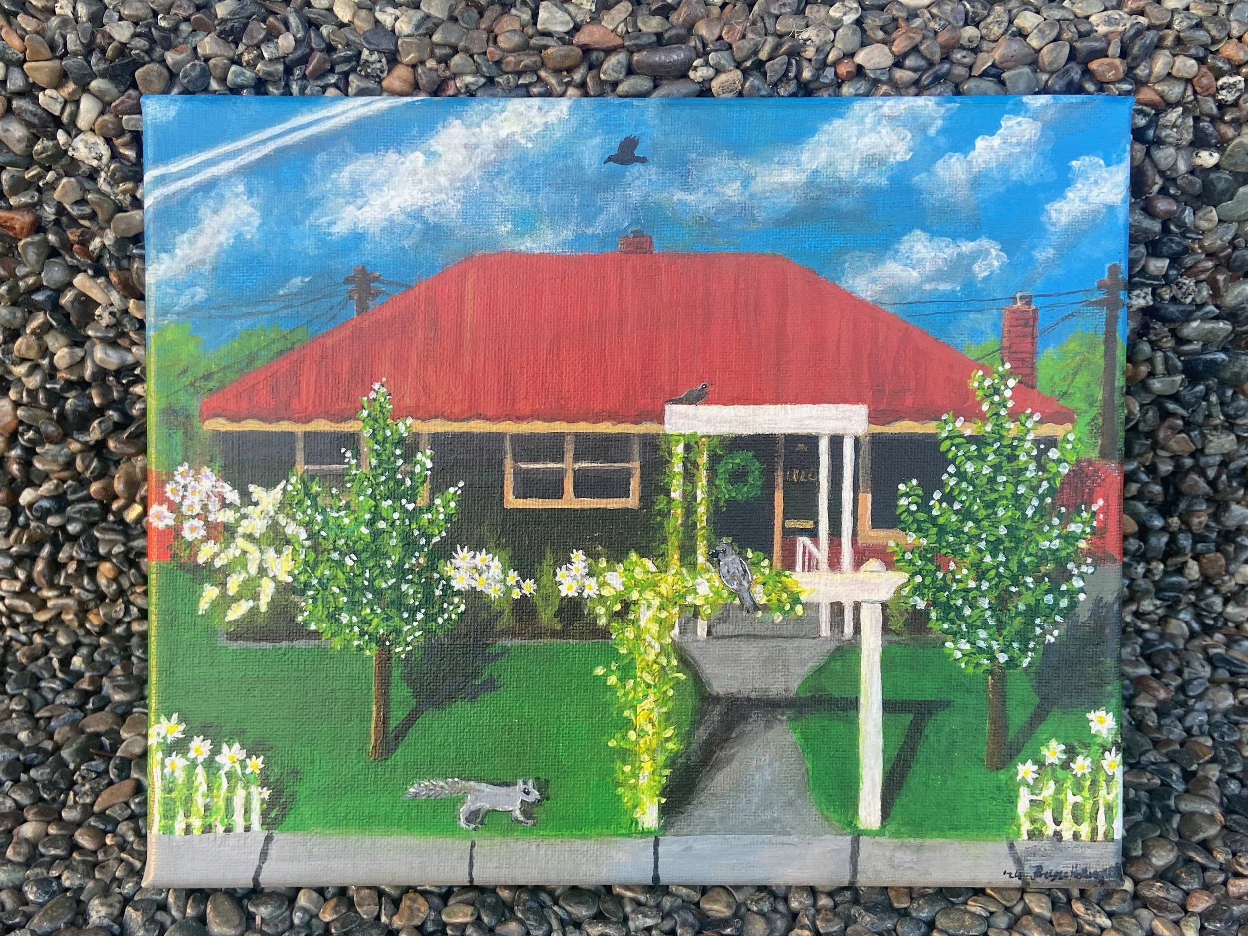 A painting of a house with a red roof, surrounded by flowering trees and a green yard, with a squirrel on the lawn and birds perched on the bushes and roof. The sky is blue with white clouds.
