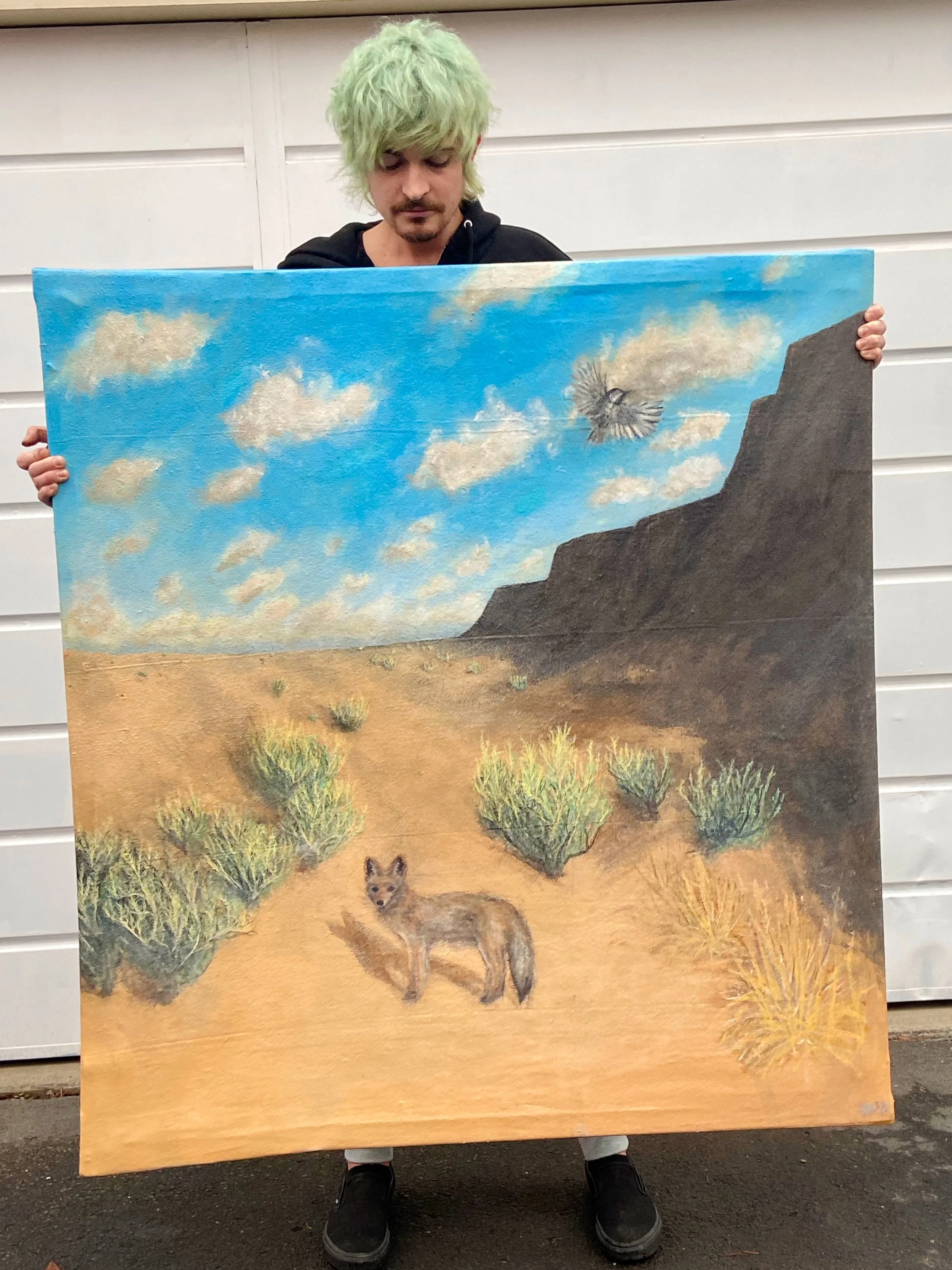 A person with light green hair holding a landscape painting depicting a desert scene with a coyote, bushes, a cliff, a cloudy sky, and a flying bird.