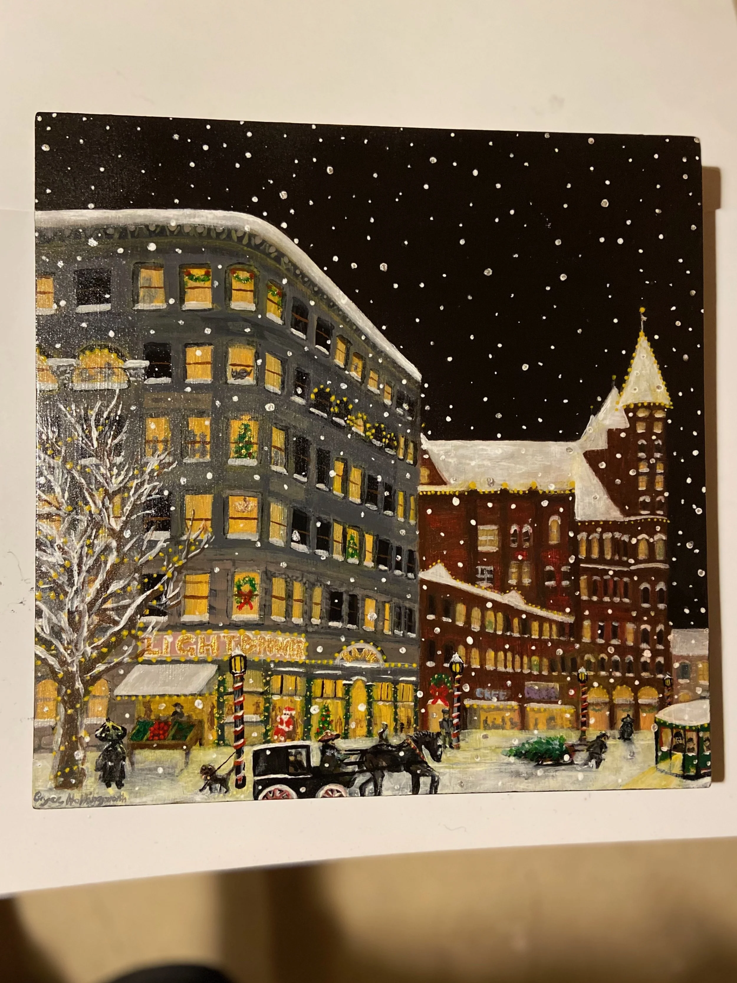 Christmas scene of a snowy city street at night with decorated shops and buildings, horse-drawn carriages, and falling snow.