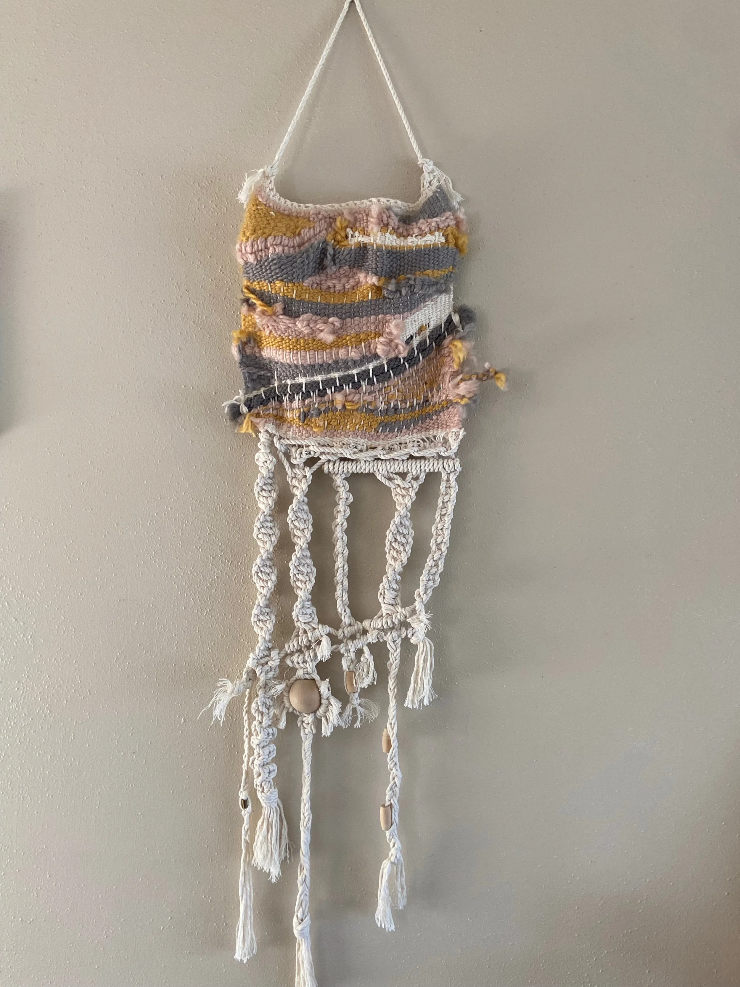 Handwoven wall hanging with a fabric top and knotted white cord fringe with shells.