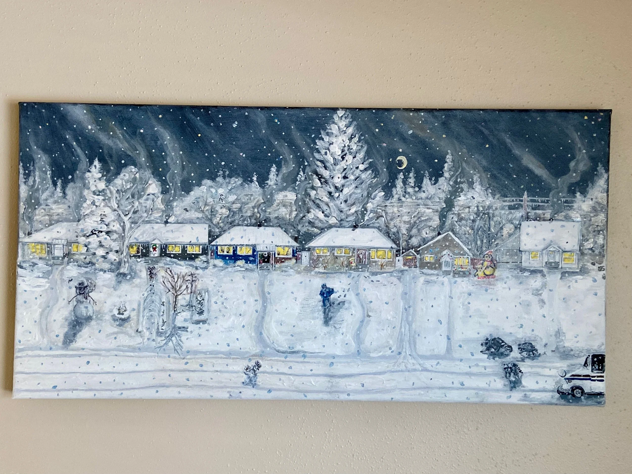 A snowy winter scene painting showing a row of houses with lit windows, a large tree, and smaller trees covered in snow. Snow is falling, and a person is walking through the snow in the foreground. The background features a dark, starry night sky wit