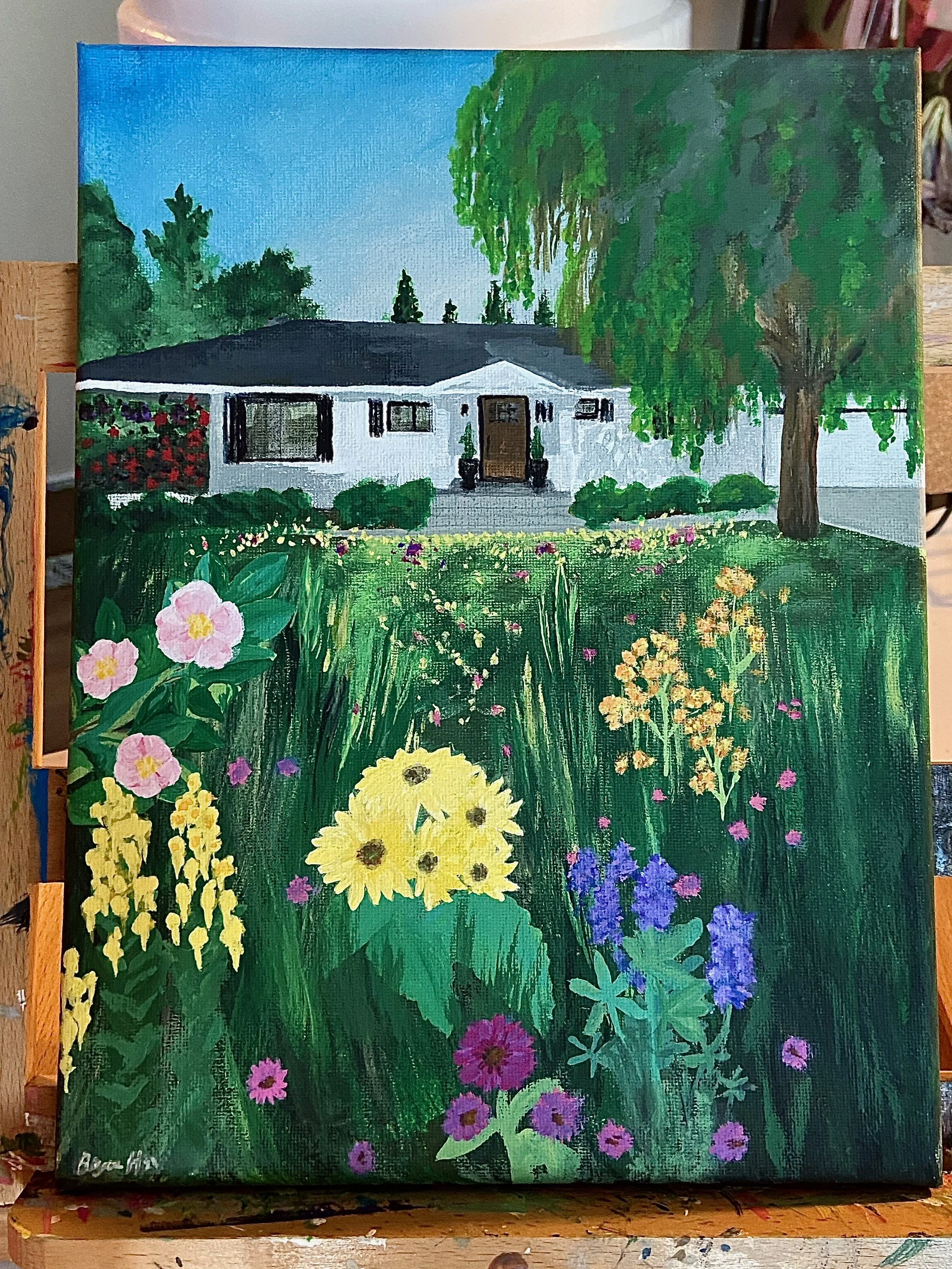 A painting of a white house with a black roof and front door, surrounded by lush greenery and colorful flowers, including pink, yellow, purple, and blue blossoms in the foreground.