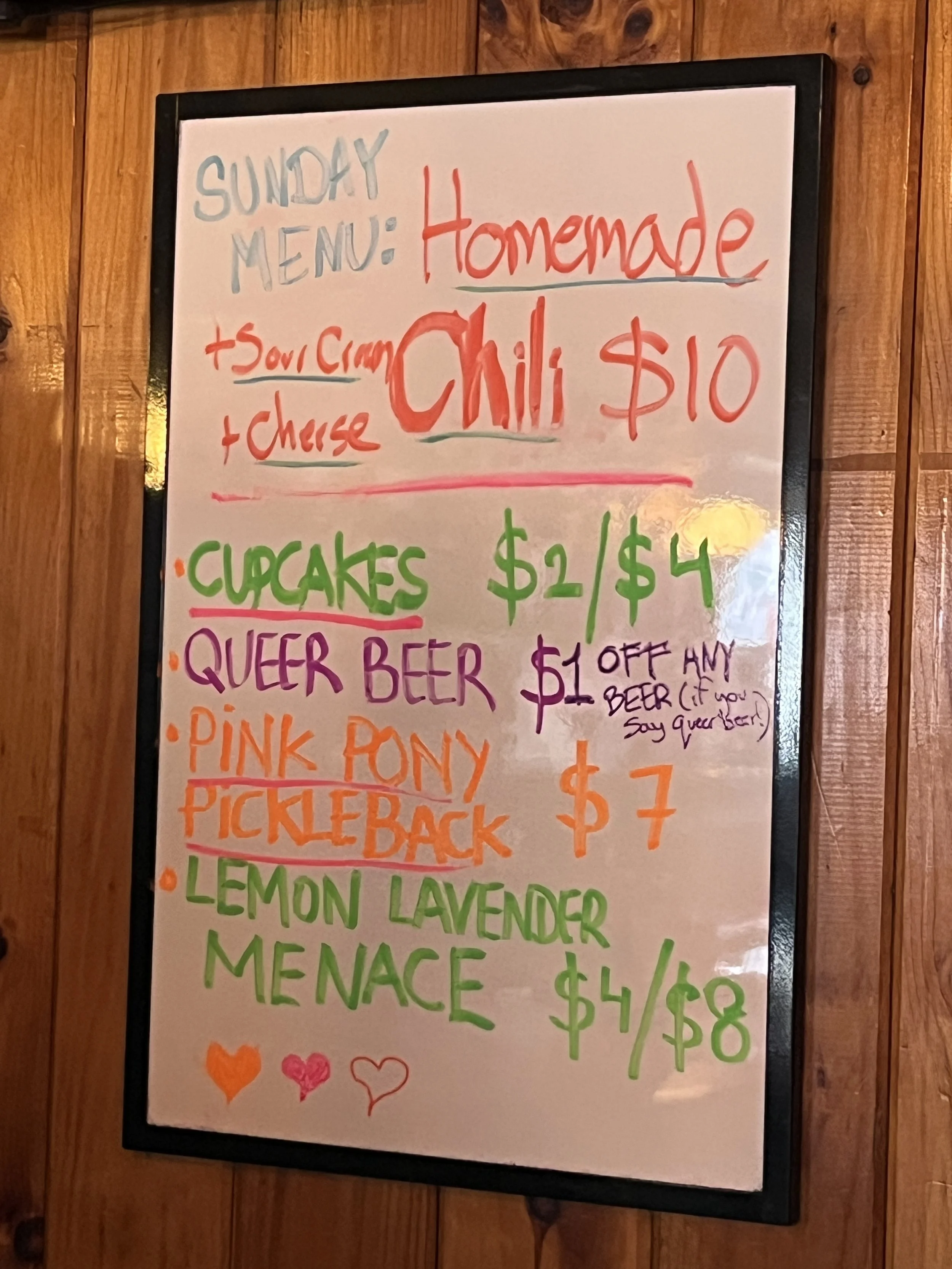 Whiteboard menu listing homemade chili and various items with prices, decorated with hearts.