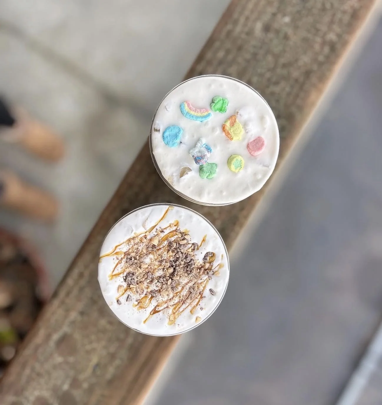 Two milkshakes topped with colorful sprinkles and caramel syrup, served on a wooden surface.