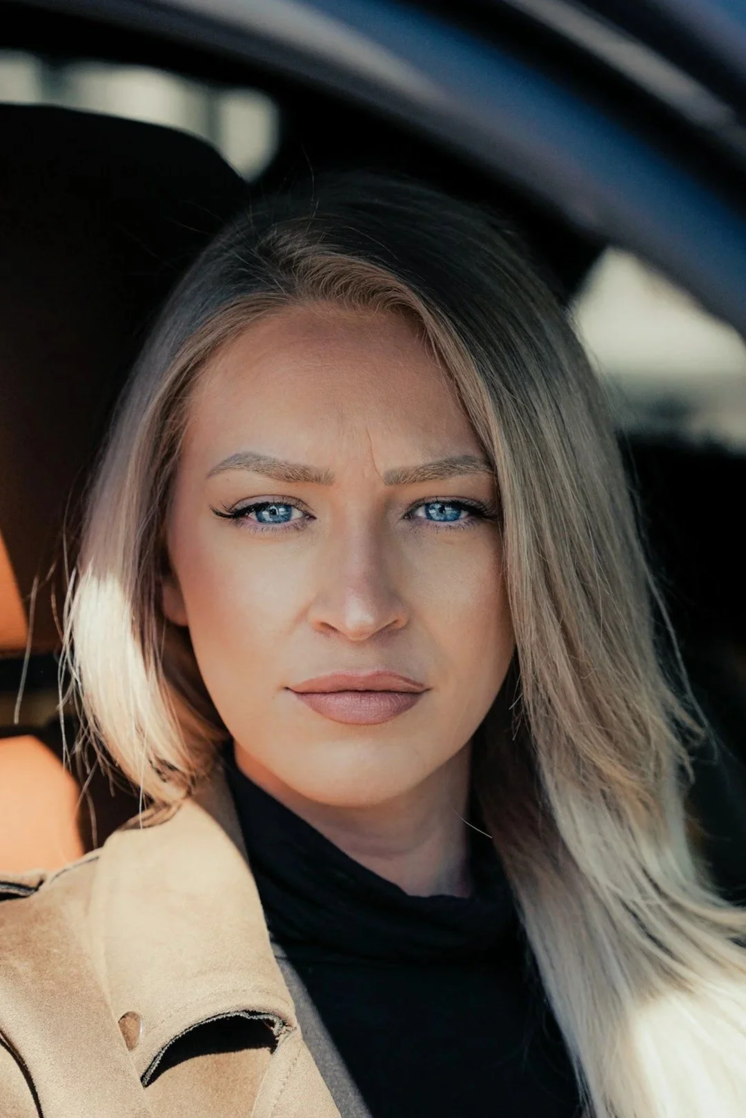 Close-up portrait of a woman with blonde hair and blue eyes sitting inside a vehicle.