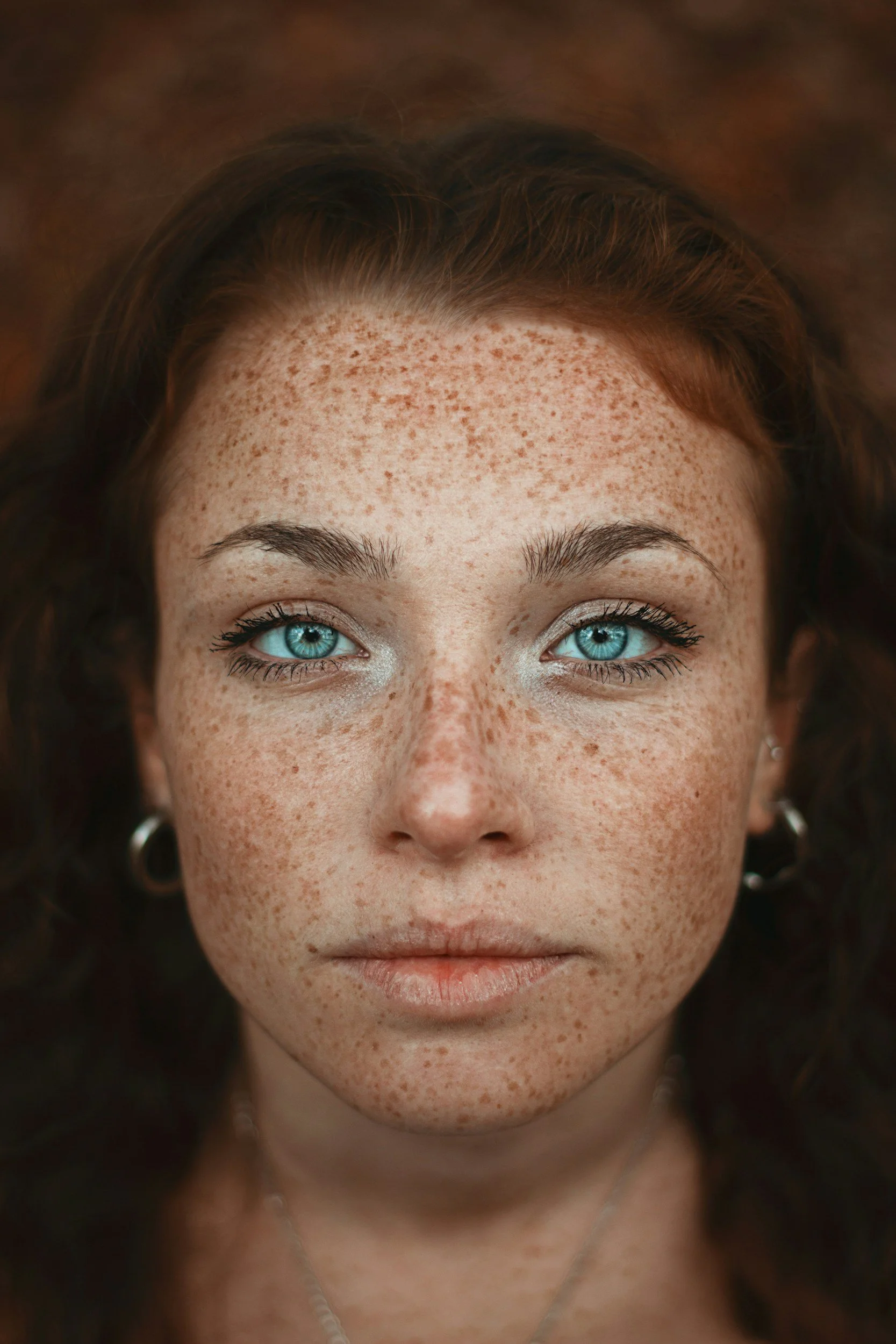 Close-up of a woman's face with striking blue eyes, red freckles, and dark wavy hair.