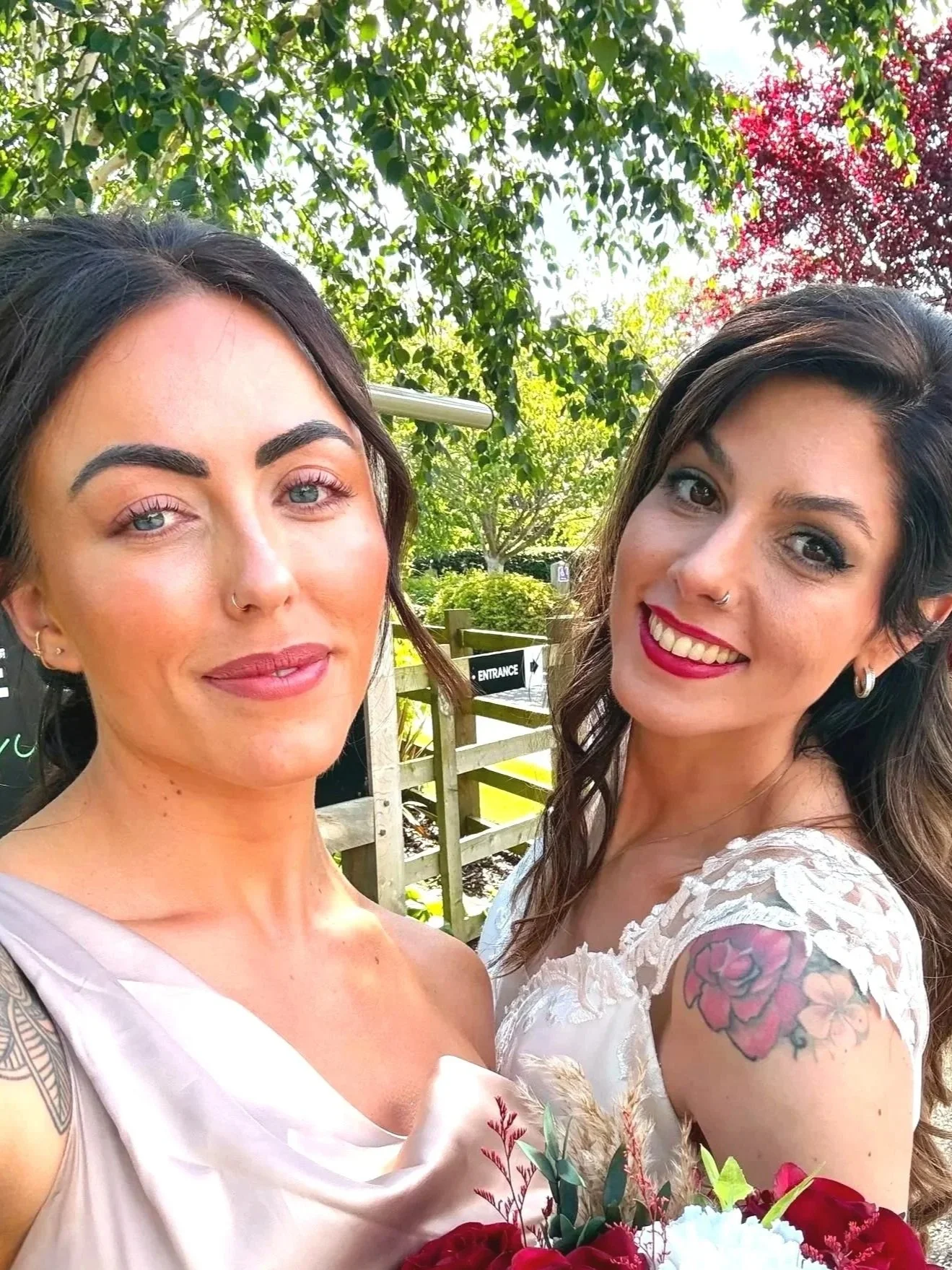 Two women smiling in a sunlit outdoor setting, embodying the calm, confident, and empowered spirit of a Triana Aesthetics bride on her special day.