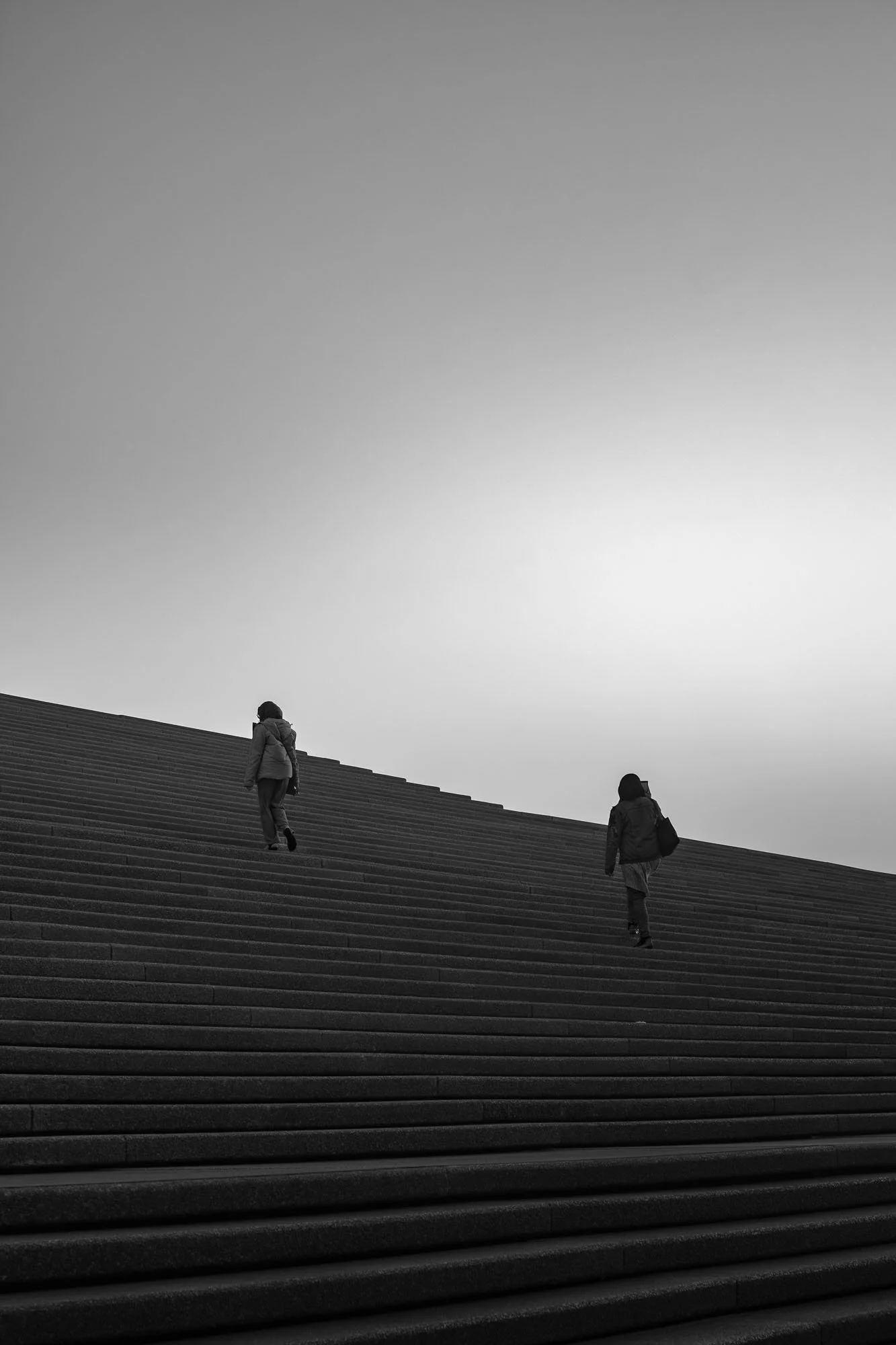 Three people walking up a large outdoor staircase against a gray sky.