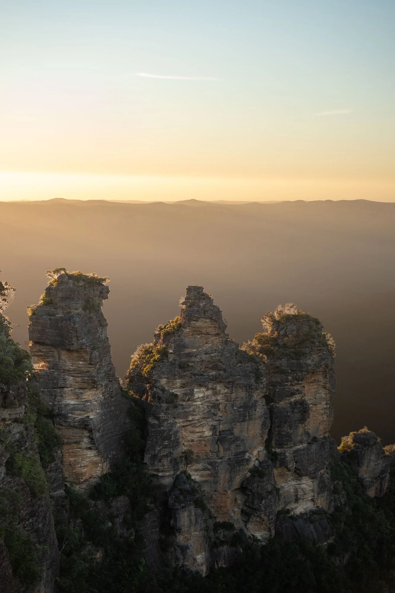 Tall rocky cliffs with trees growing on top, set against a hazy background with a flat horizon and a bright sky.