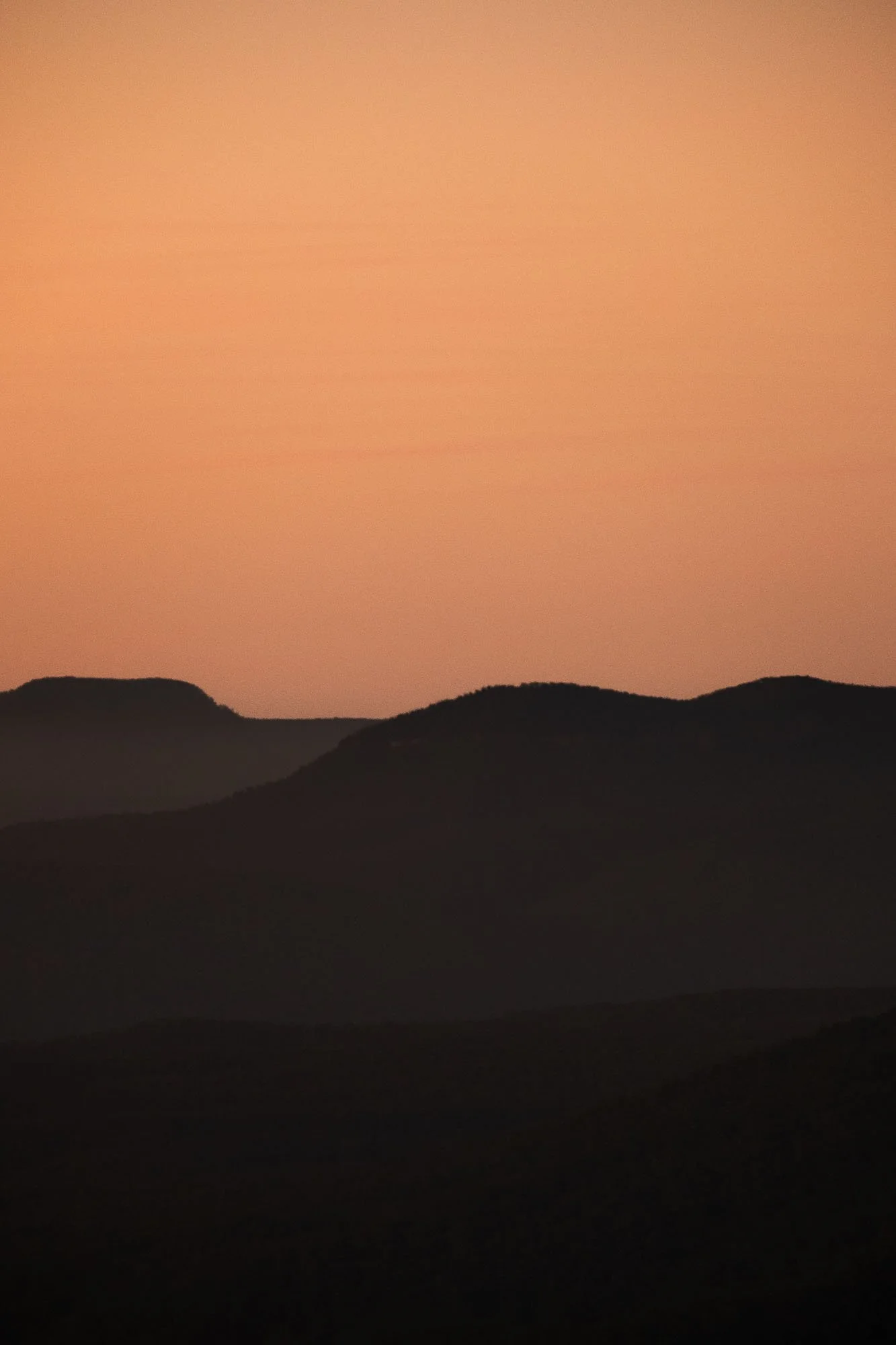 Silhouettes of mountains at sunset with an orange sky.