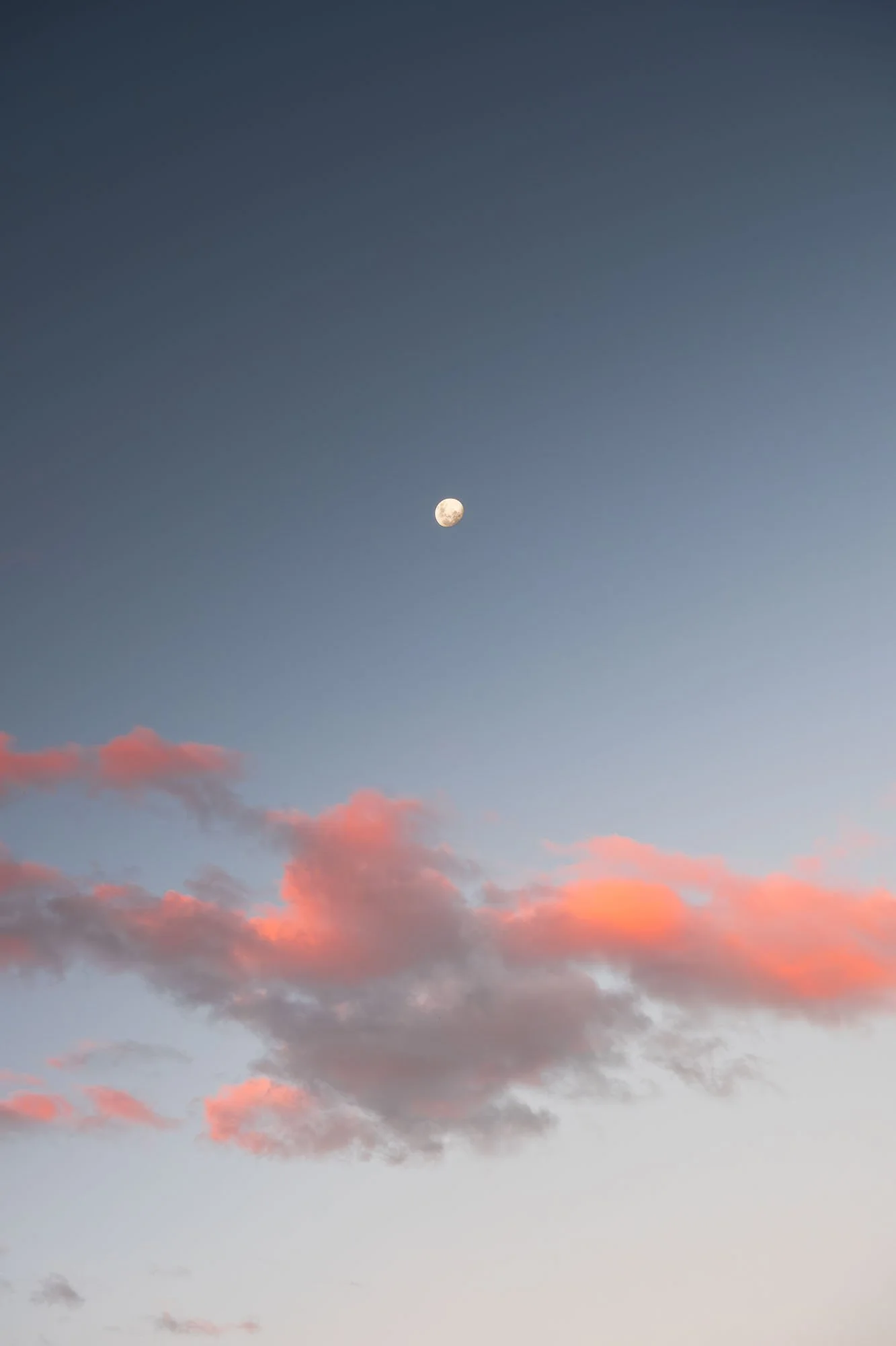 The moon in a clear evening sky with scattered pink clouds near the horizon.