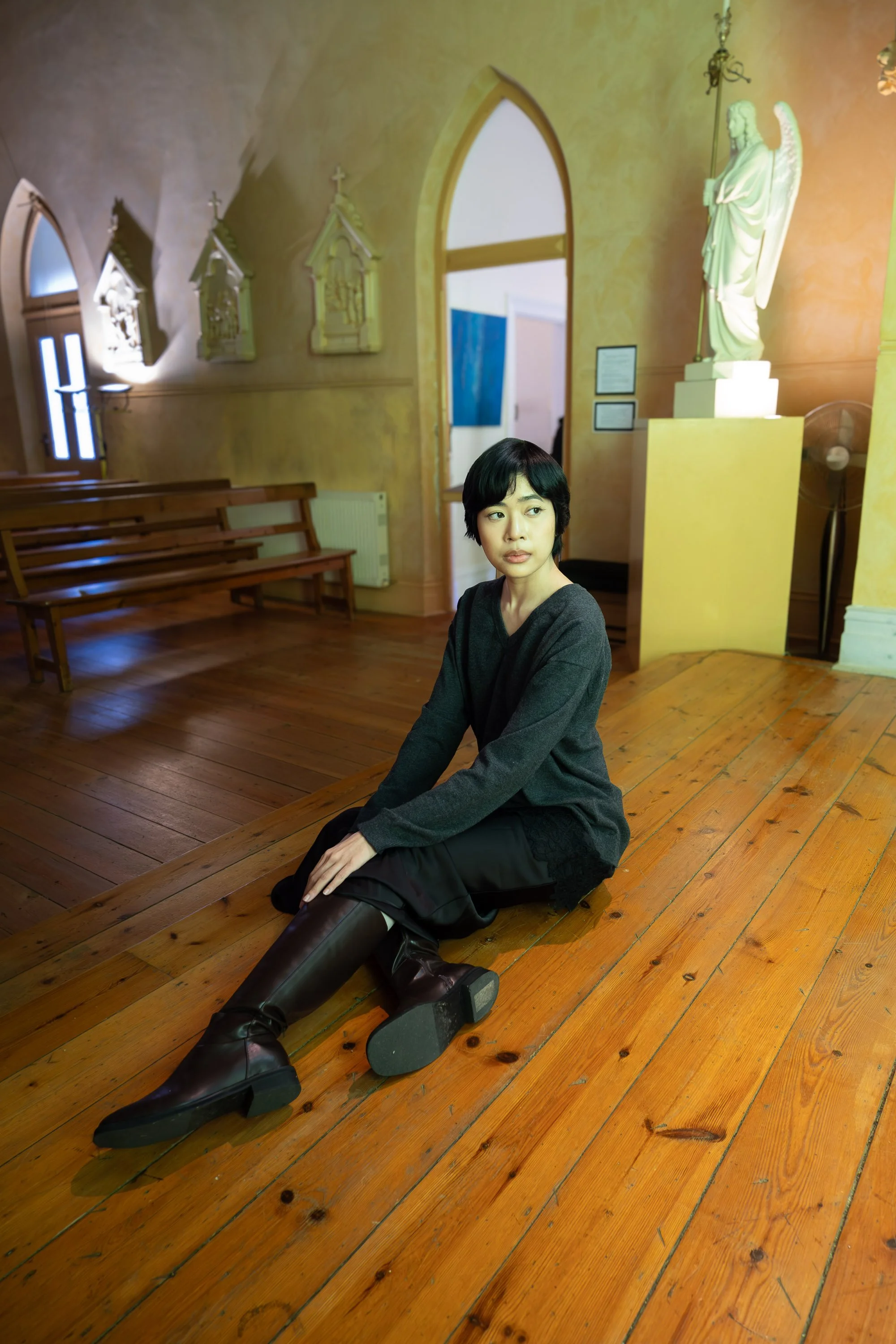 A woman sitting on a wooden floor inside a church, with religious statues and artwork on the walls behind her.