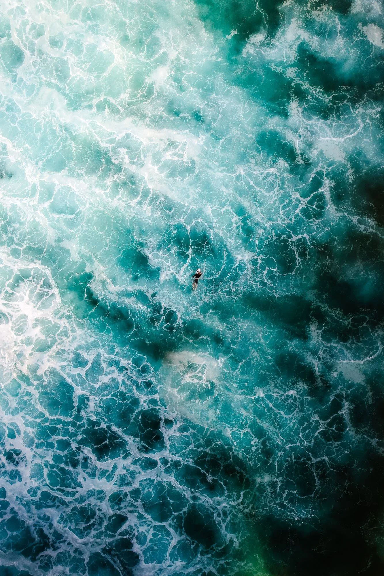 Overhead view of a person surfing in the ocean with waves and white foam.
