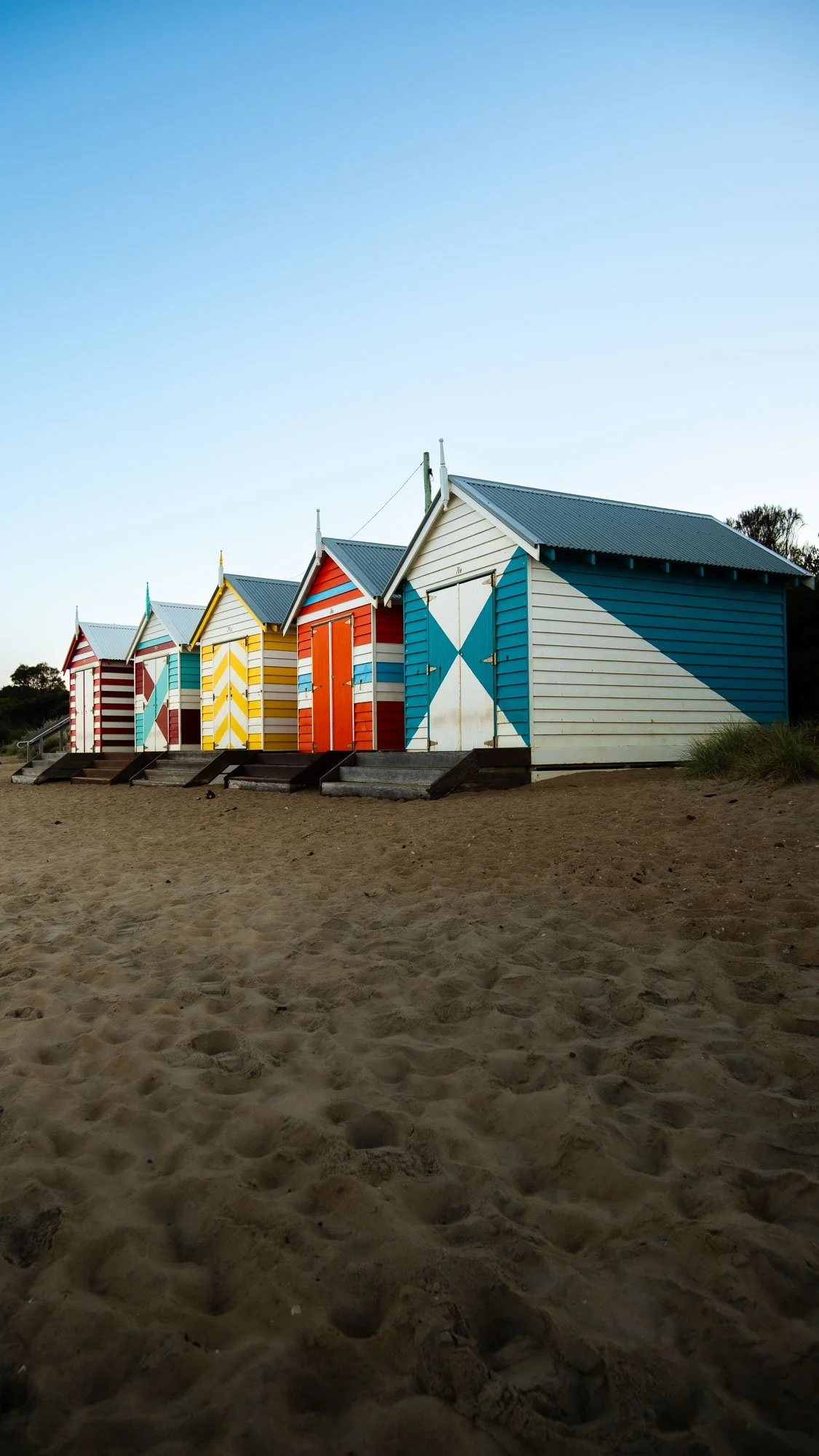 Colorful beach huts lined up on the sand, with a clear blue sky above.