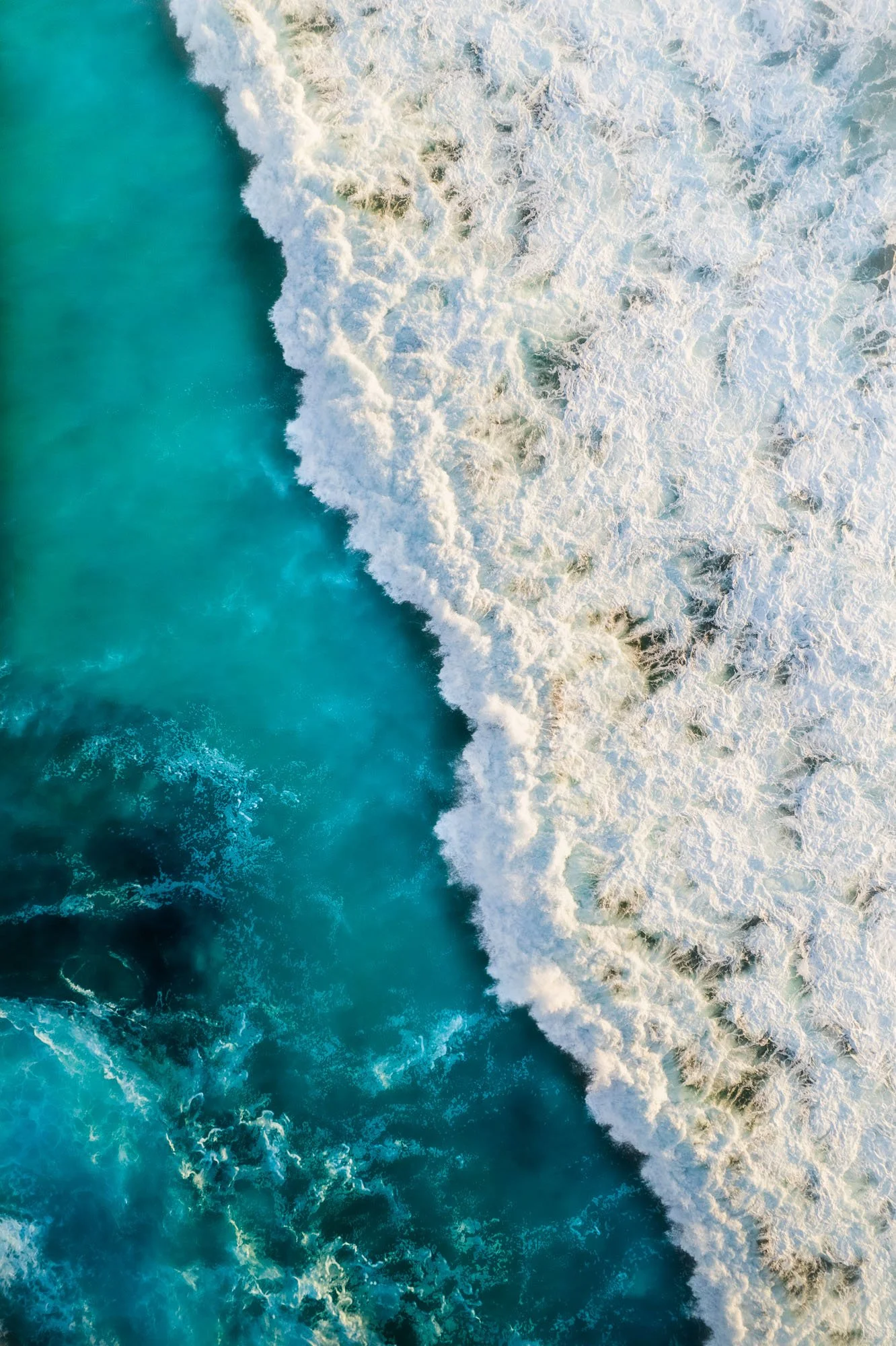Aerial view of ocean waves crashing onto turquoise water.