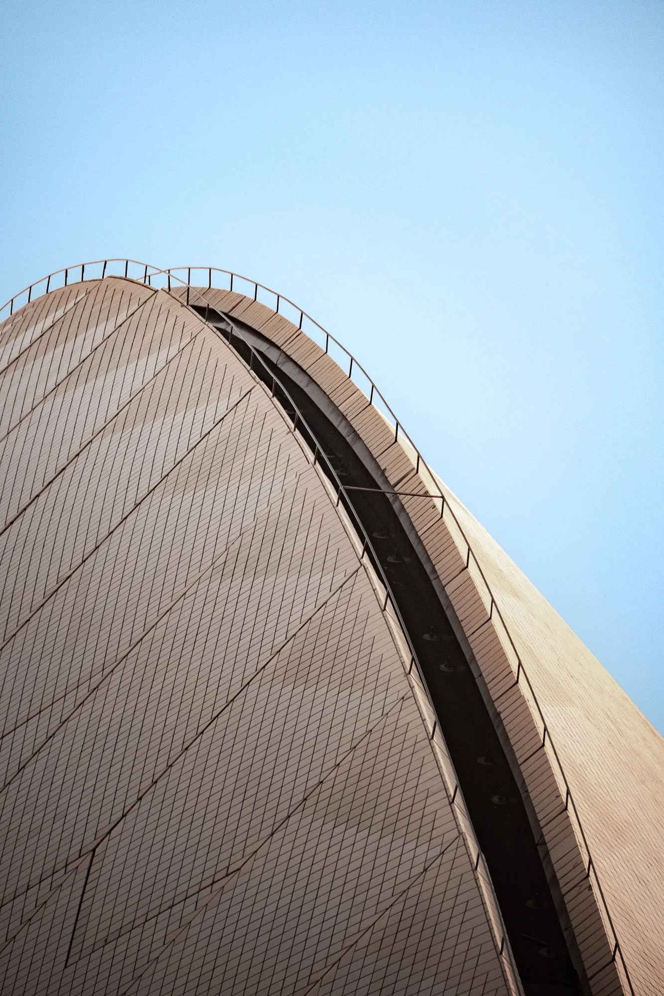 Close-up of the Sydney Opera House with its distinct shell-like design and tiled exterior against a clear blue sky.
