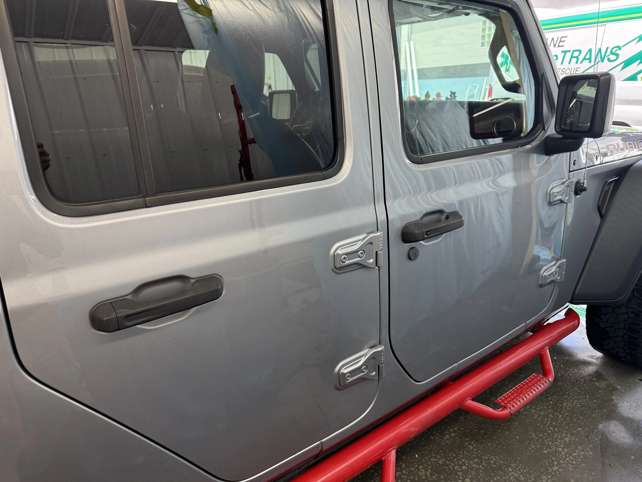 Close-up of a silver off-road vehicle, possibly a Jeep, with black side mirrors and a red safety bar beside it.