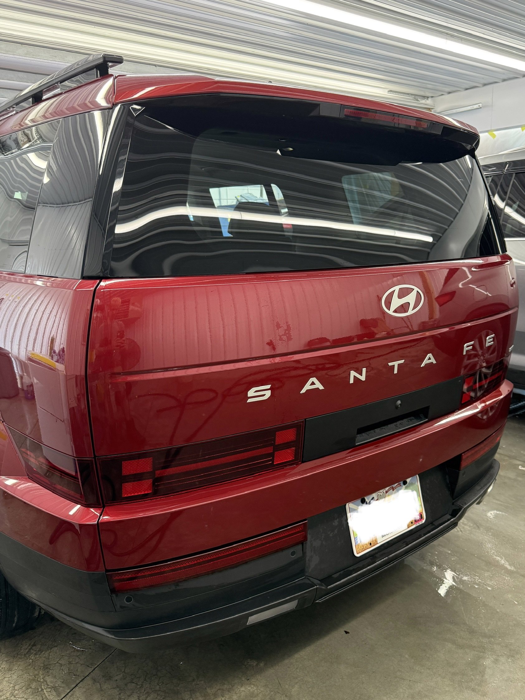 The rear of a red Hyundai Santa Fe SUV parked inside a garage, showing the back windshield, taillights, and rear bumper.