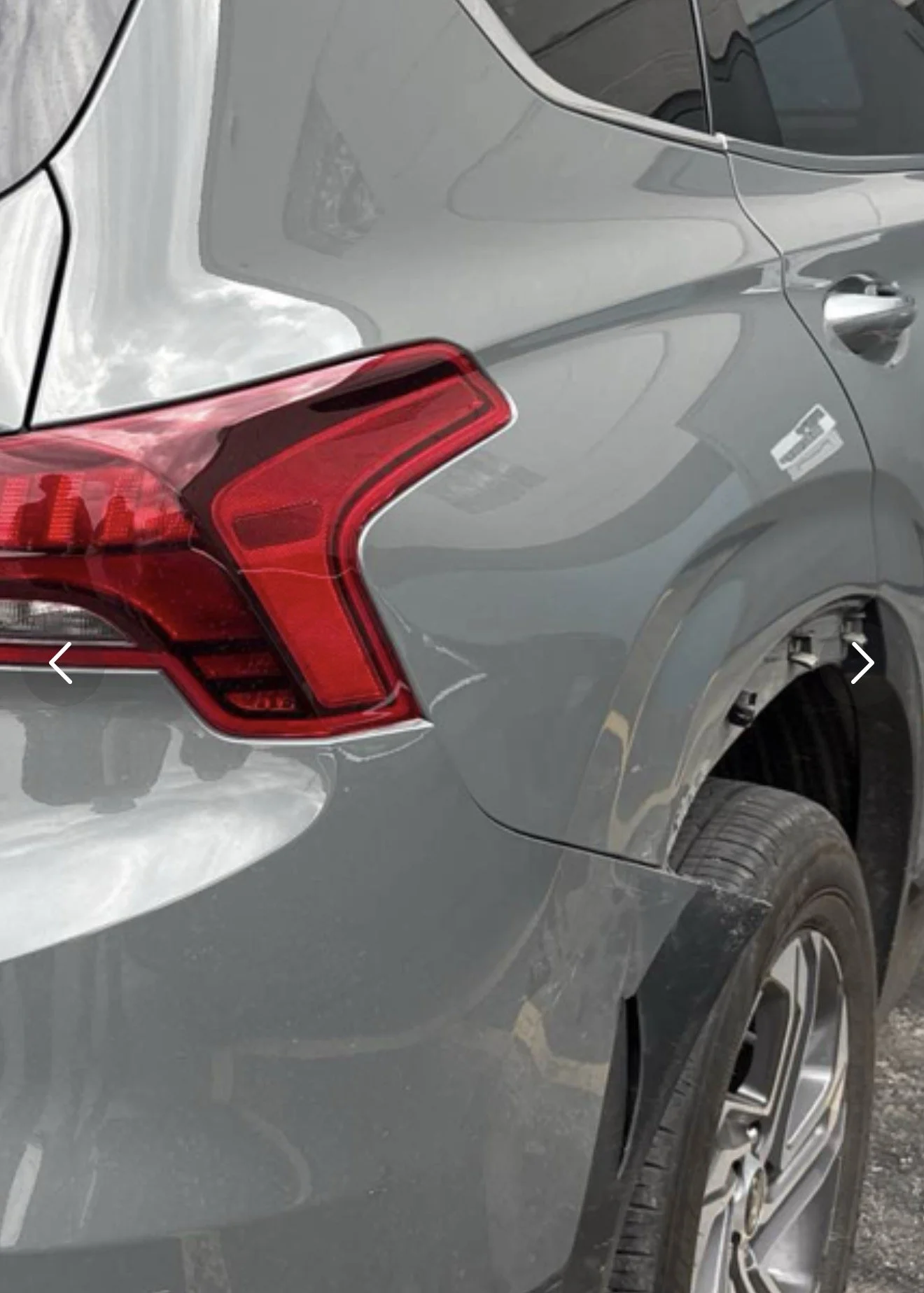 Close-up of the rear part of a gray car, showing the taillight, rear quarter panel, and part of the rear wheel.