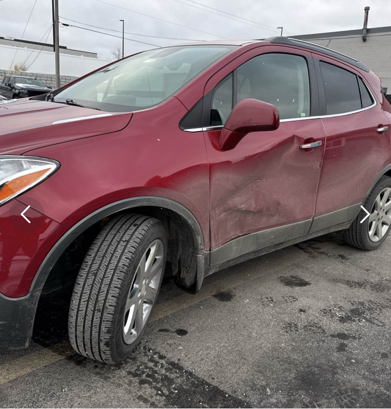 Red SUV with damaged front and rear fenders, dirty lower body, and parked on a muddy parking lot with other cars in the background.