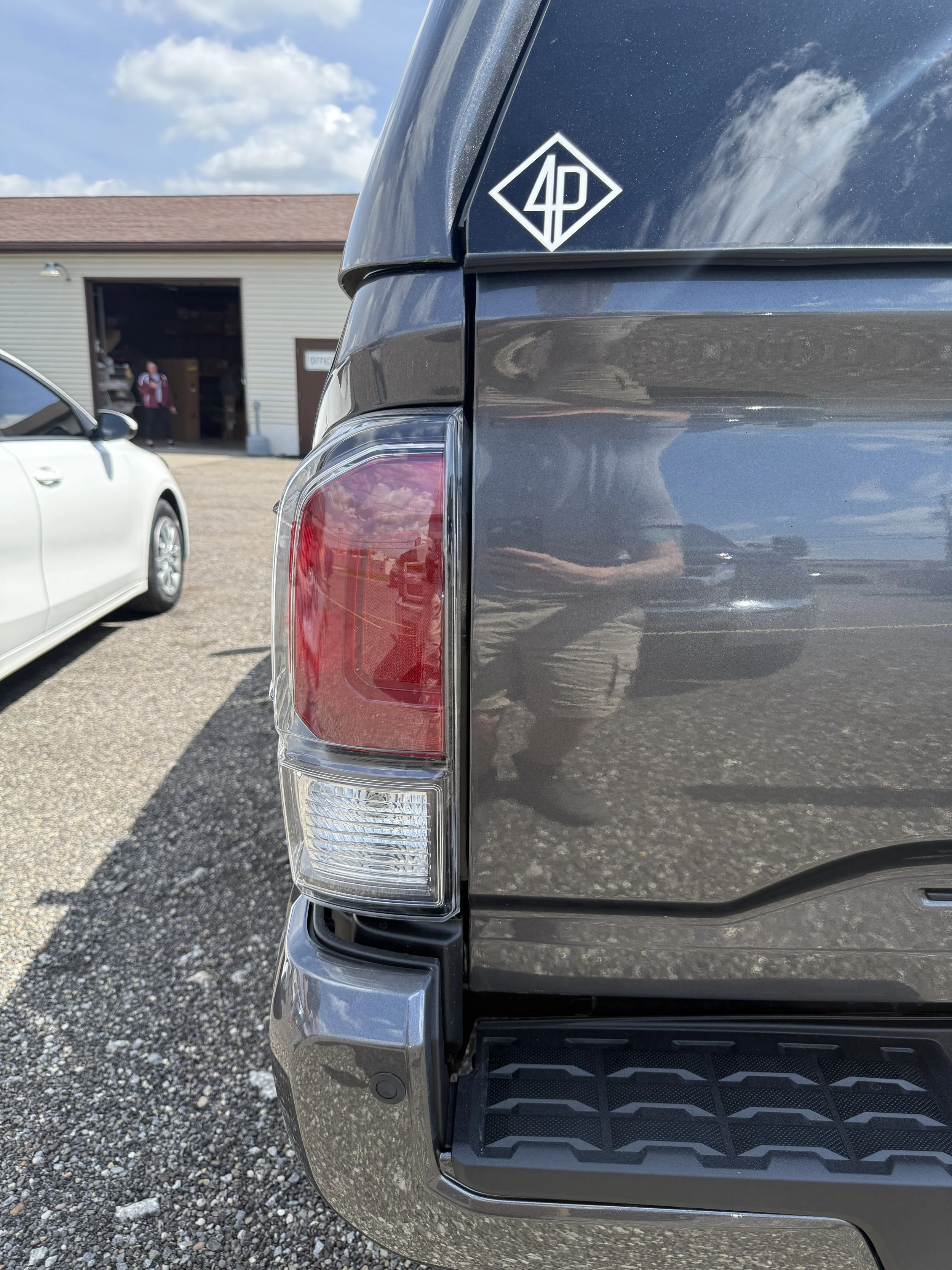 The back of a gray pickup truck with a diamond-shaped decal on the rear window that reads '4P' in stylized white lettering.
