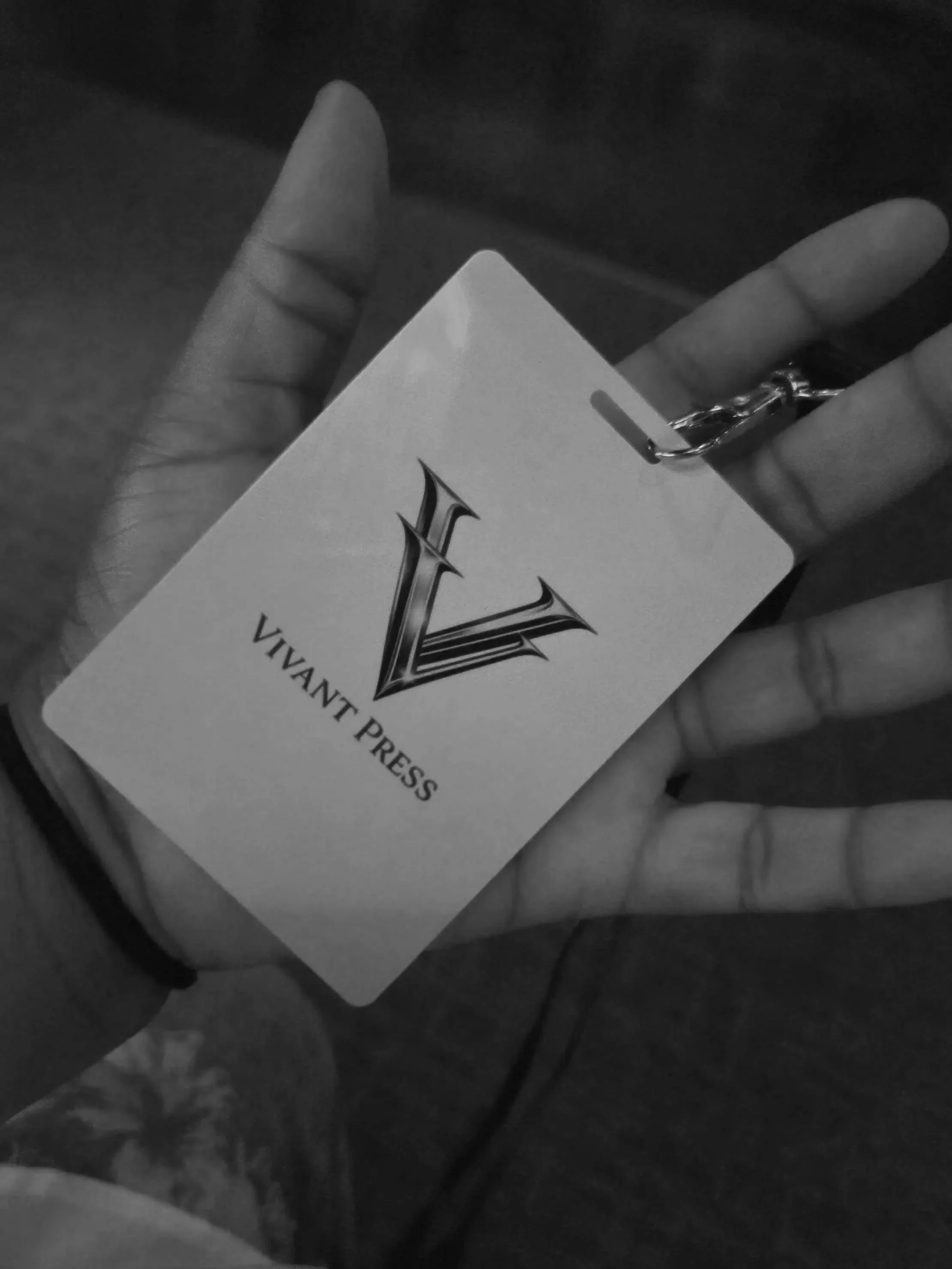 Hand holding a card with the words "VivanT Press" and a stylized letter "V" logo, with a chain attached to the card.