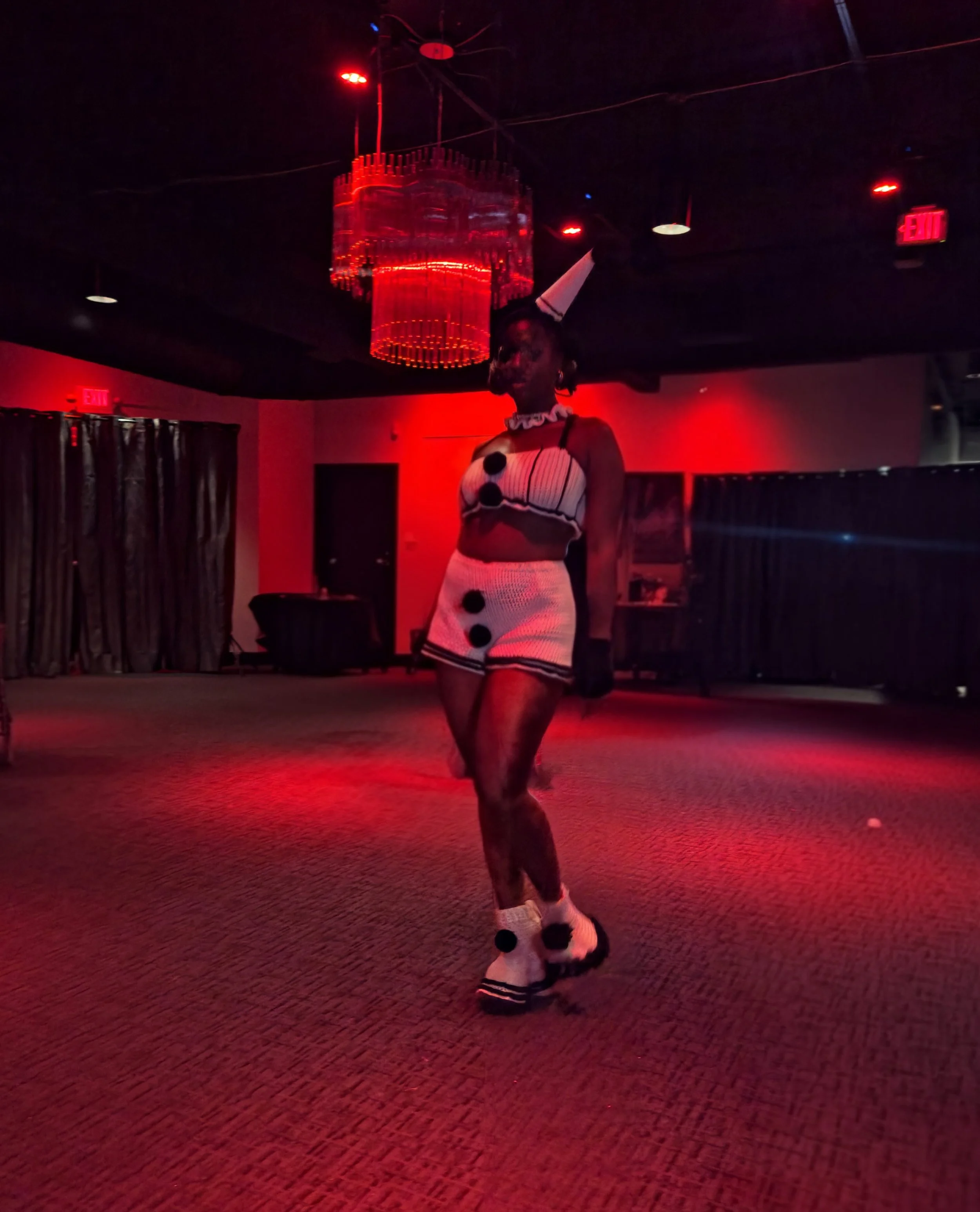 Person dressed in a cow costume standing in a dimly lit room with red lighting and a chandelier on the ceiling.