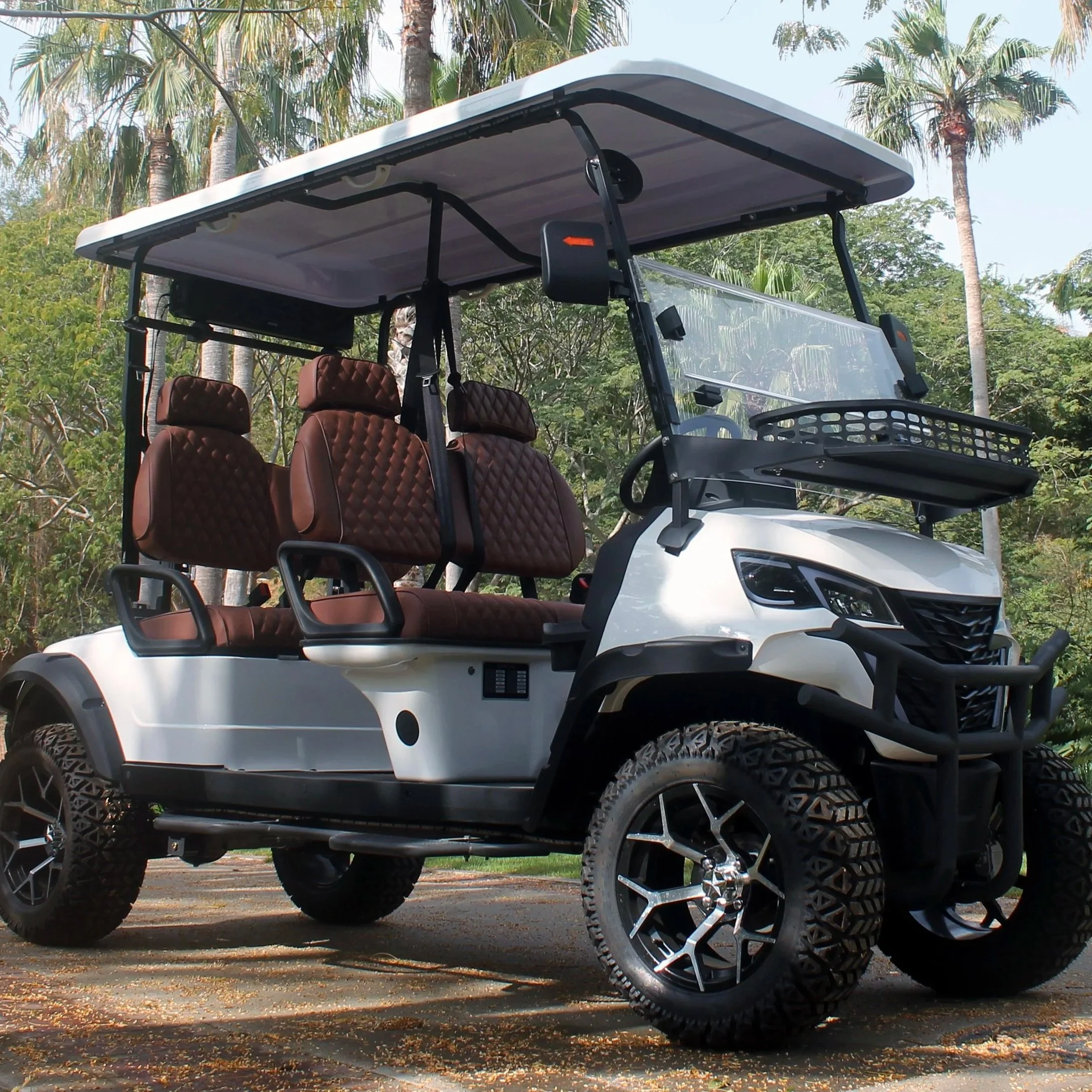 White golf cart with brown seats and large tires parked outdoors with trees in the background.