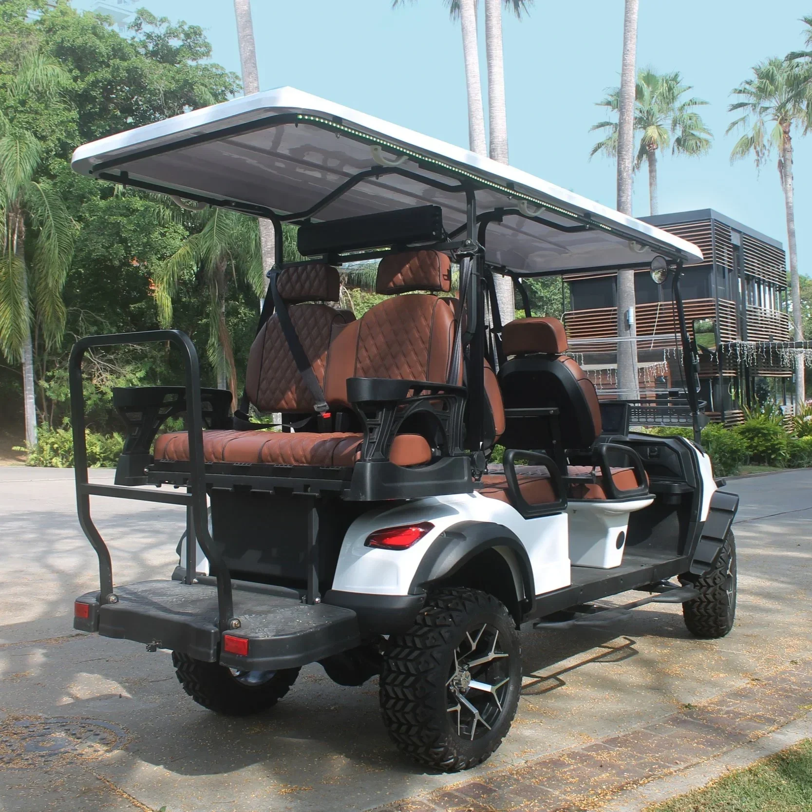 A white golf cart with brown leather seats parked on a concrete path in a lush tropical area with palm trees and a modern building in the background.