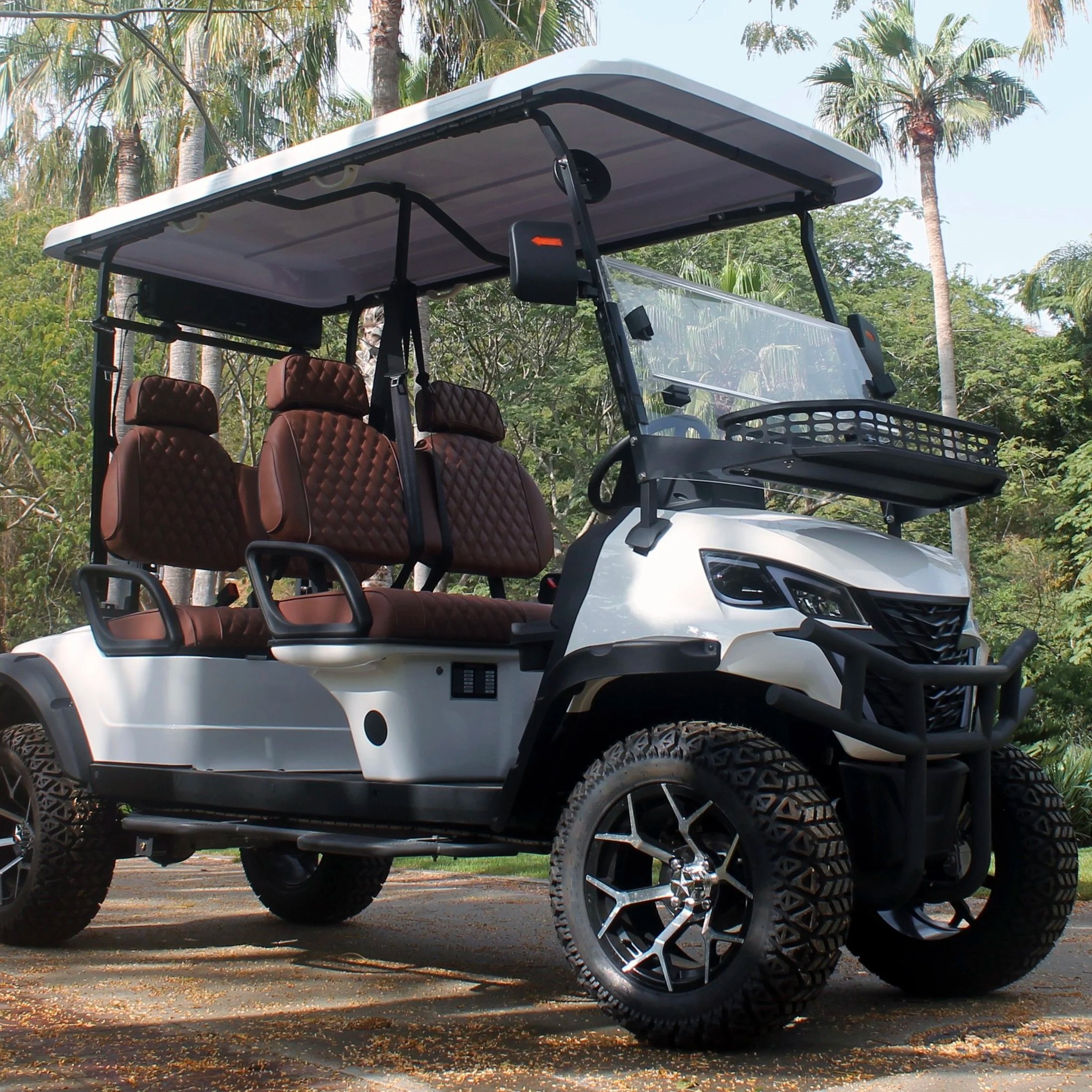 A white electric golf cart with brown quilted seats parked outdoors on a paved surface surrounded by palm trees.